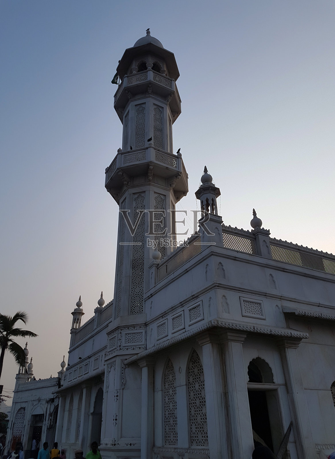 高耸的清真寺在黄昏时分展示了精美的建筑,周围人们在繁忙的城市环境中交谈。照片摄影图片