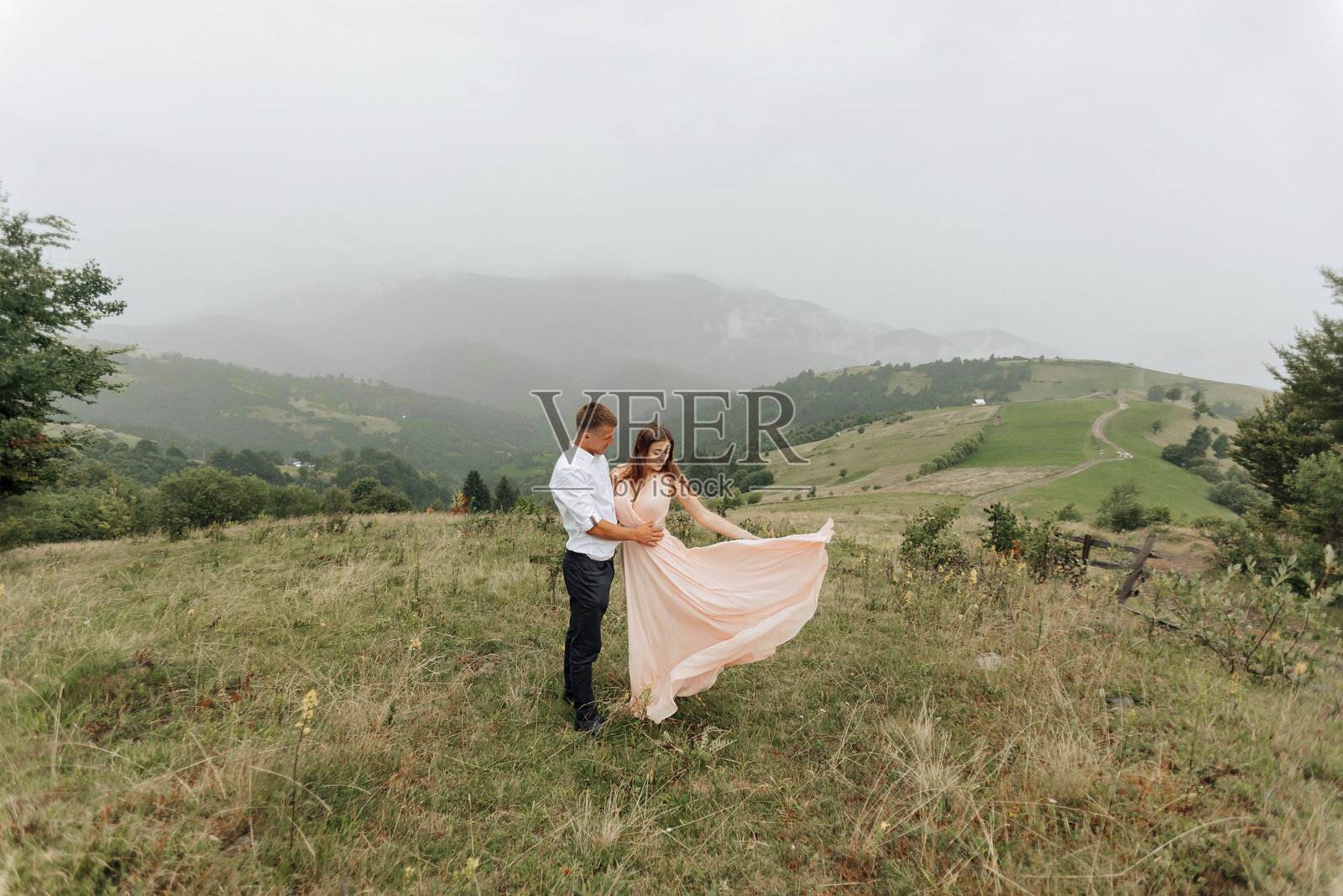 一对情侣站在田野里,女人穿着粉色连衣裙。照片摄影图片