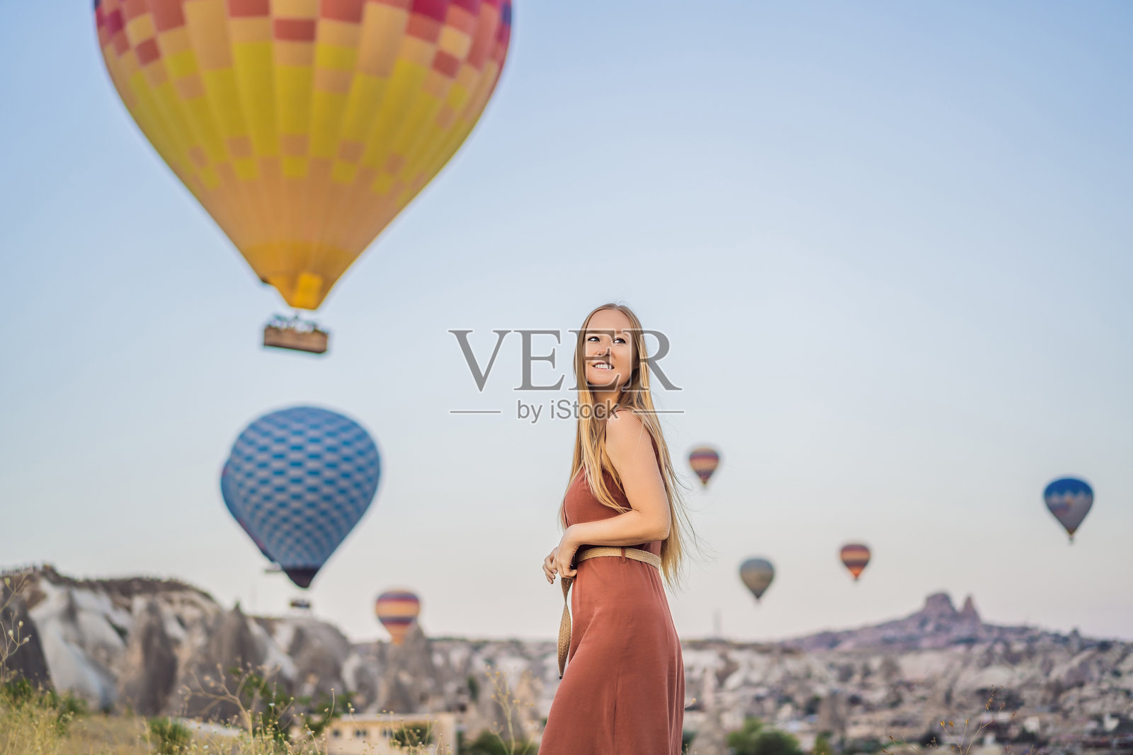 在土耳其卡帕多奇亚,一位女游客欣赏热气球。快乐的土耳其旅行概念。女子在山顶享受美妙的景色。照片摄影图片