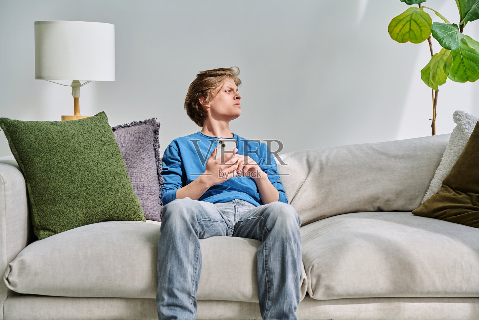 帅气严肃的少年在家沙发上坐着,手里拿着智能手机照片摄影图片