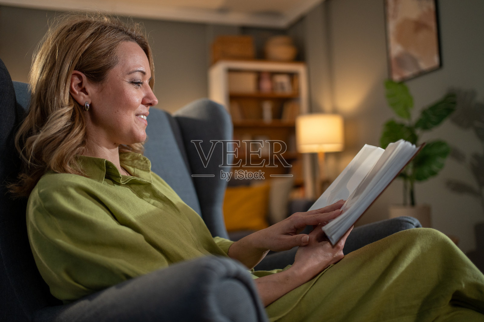 微笑的女性在家中的扶手椅上阅读一本书照片摄影图片