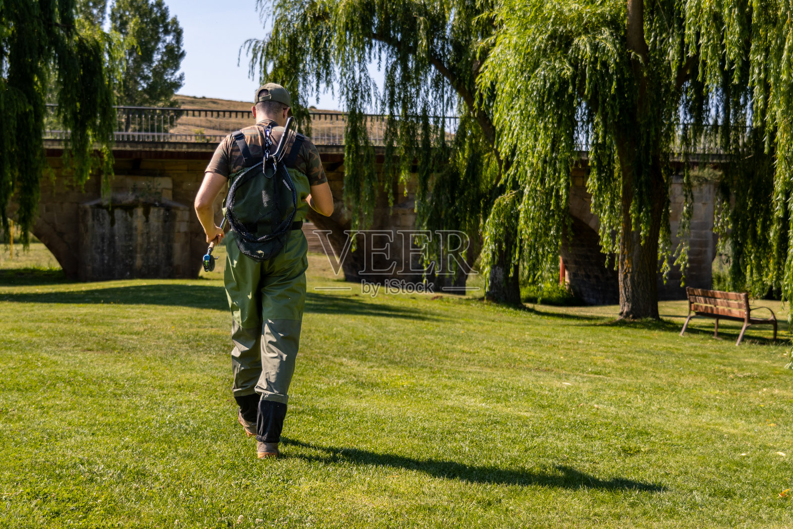 渔夫走在草地上,朝着河流和桥走去照片摄影图片