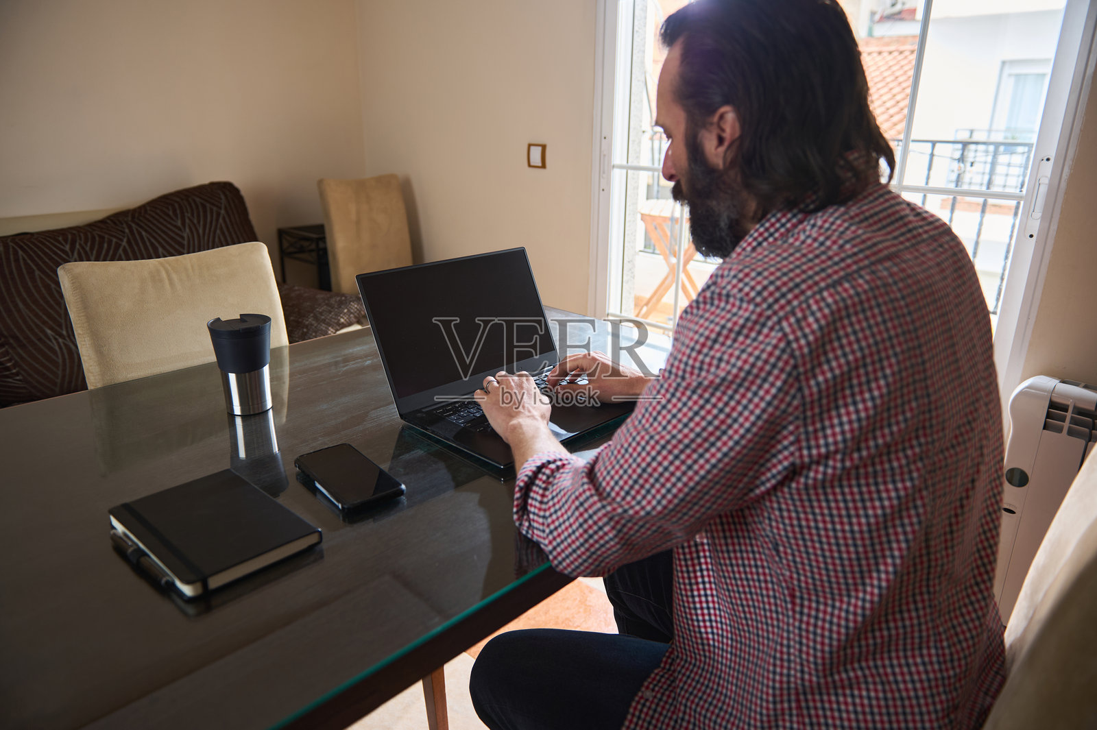 在家用笔记本电脑工作的男人,旁边有笔记本和杯子照片摄影图片