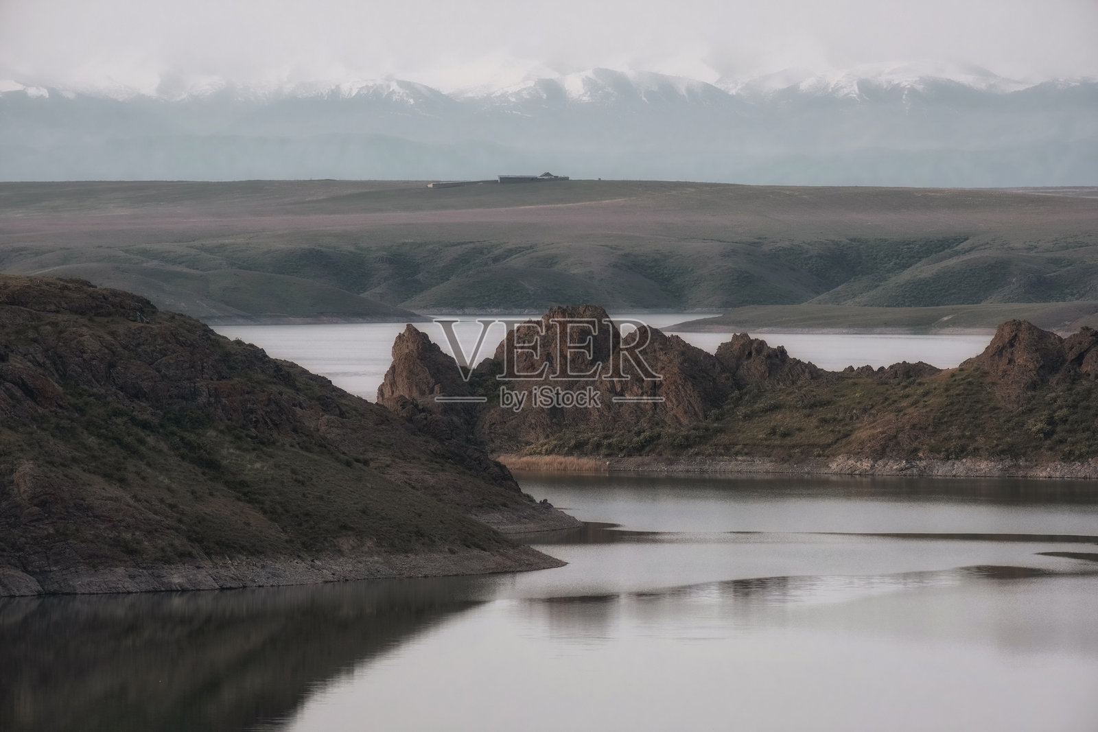 哈萨克斯坦库尔廷斯科水库的海岸上耸立着戏剧性的岩石突起,远处的地平线上可见白雪皑皑的山脉。一个宁静而美丽的自然风光。照片摄影图片