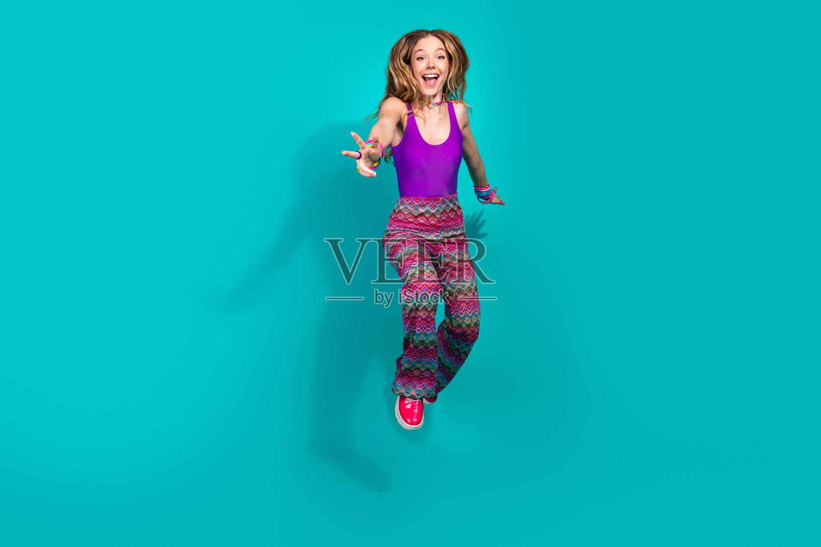 年轻女性穿着复古服装在青绿色背景下快乐地跳舞,体现了乐趣和活力。照片摄影图片