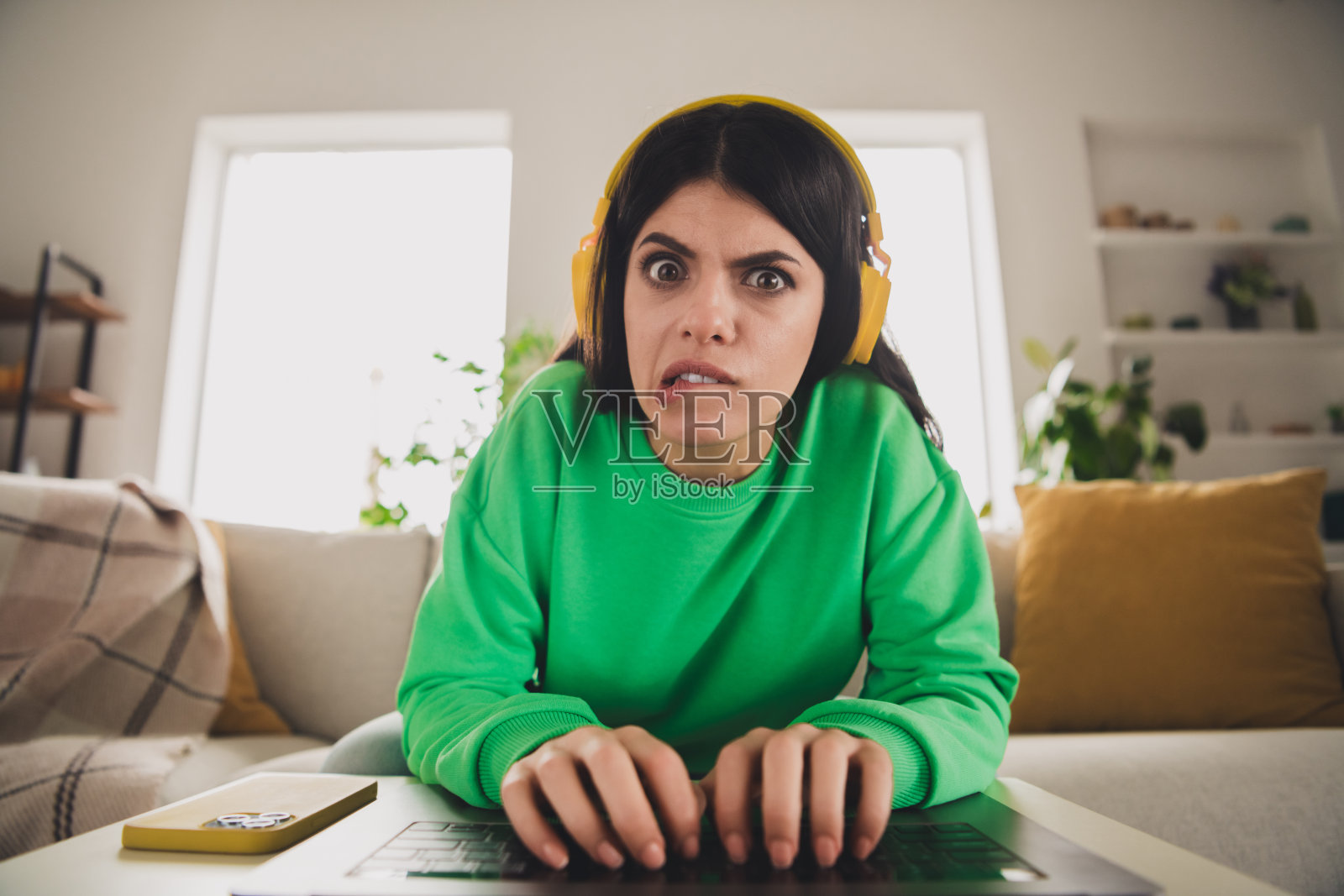 年轻女性穿着休闲的绿色卫衣,坐在阳光明媚的现代舒适客厅中,面露困惑。照片摄影图片