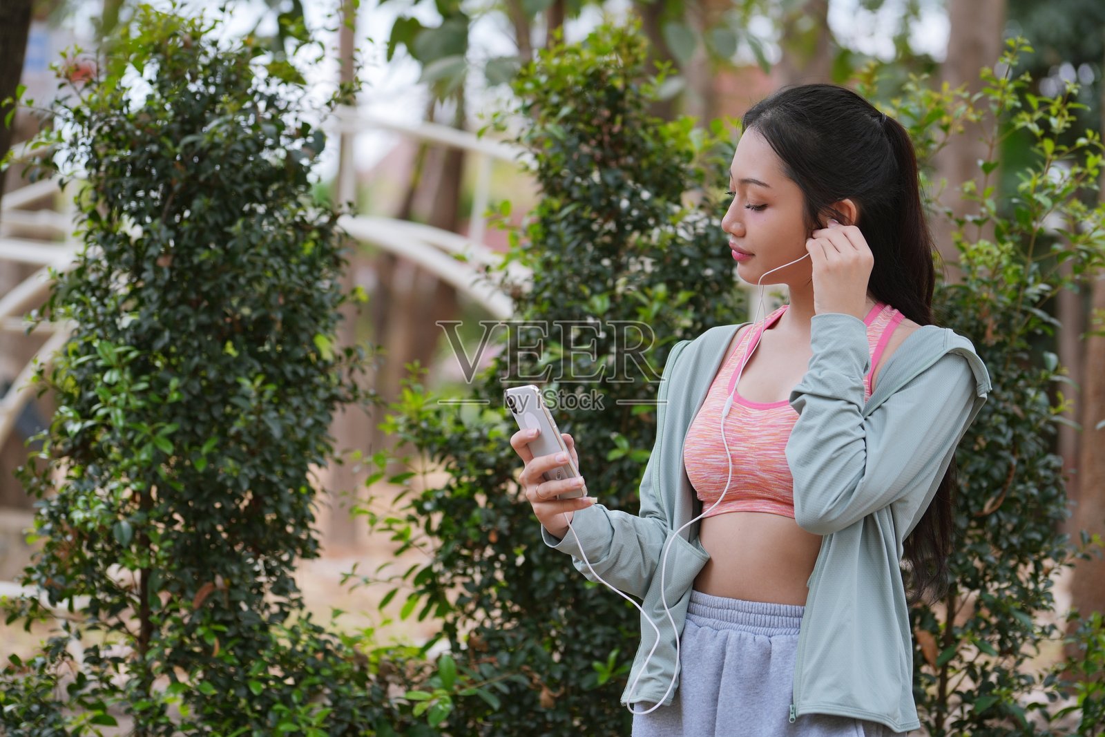 身材健美的年轻亚洲女性在绿色自然公园户外使用手机查看健身应用程序。照片摄影图片