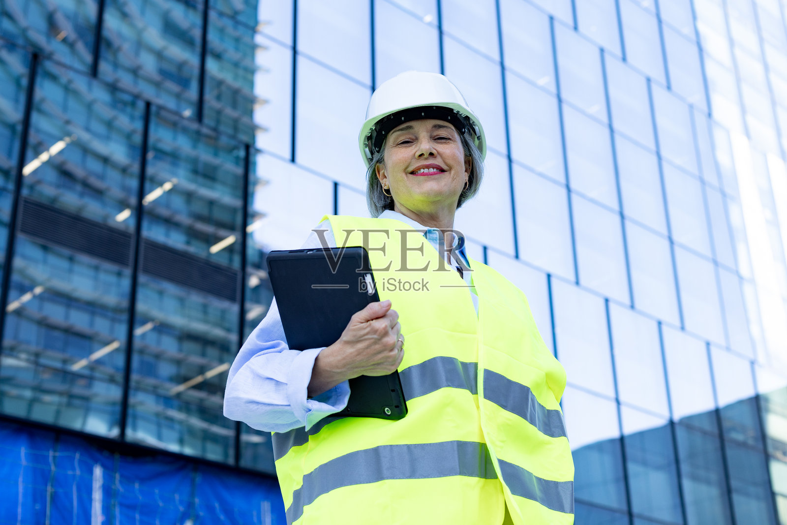 微笑的女性工程师在现代建筑前手持平板电脑照片摄影图片