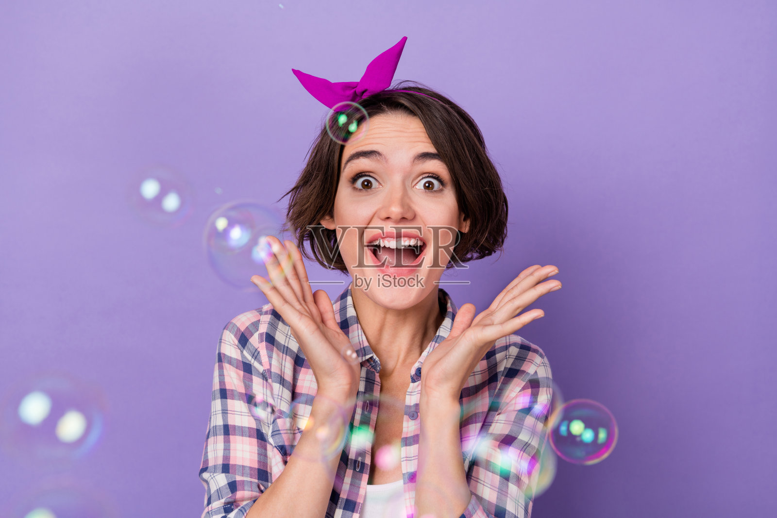 年轻兴奋可爱的女孩在紫色背景下玩耍,心情愉悦,享受泡泡的乐趣。照片摄影图片