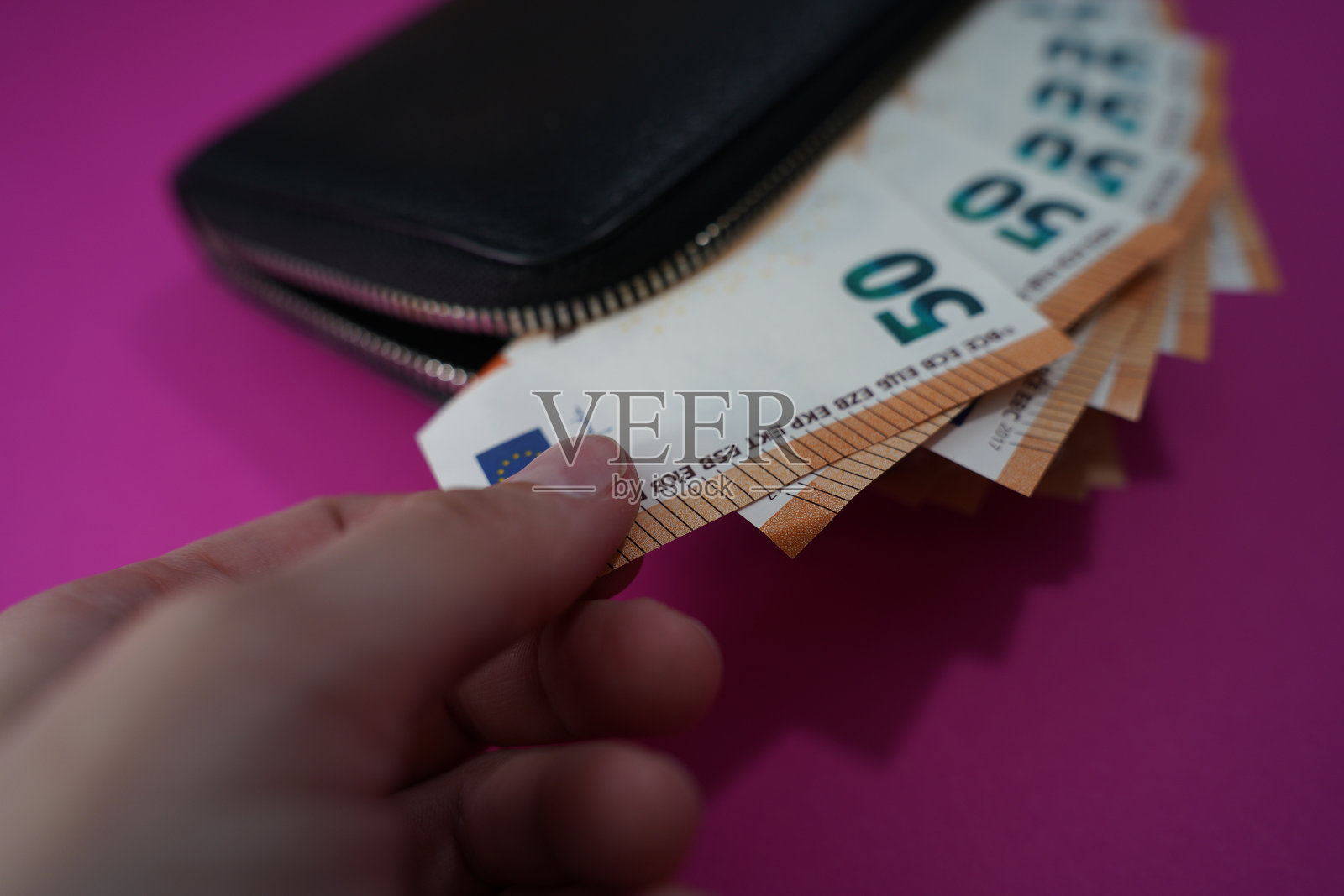 一只手从黑色钱包中抽出50欧元钞票,背景为粉色,涉及金融和消费。照片摄影图片