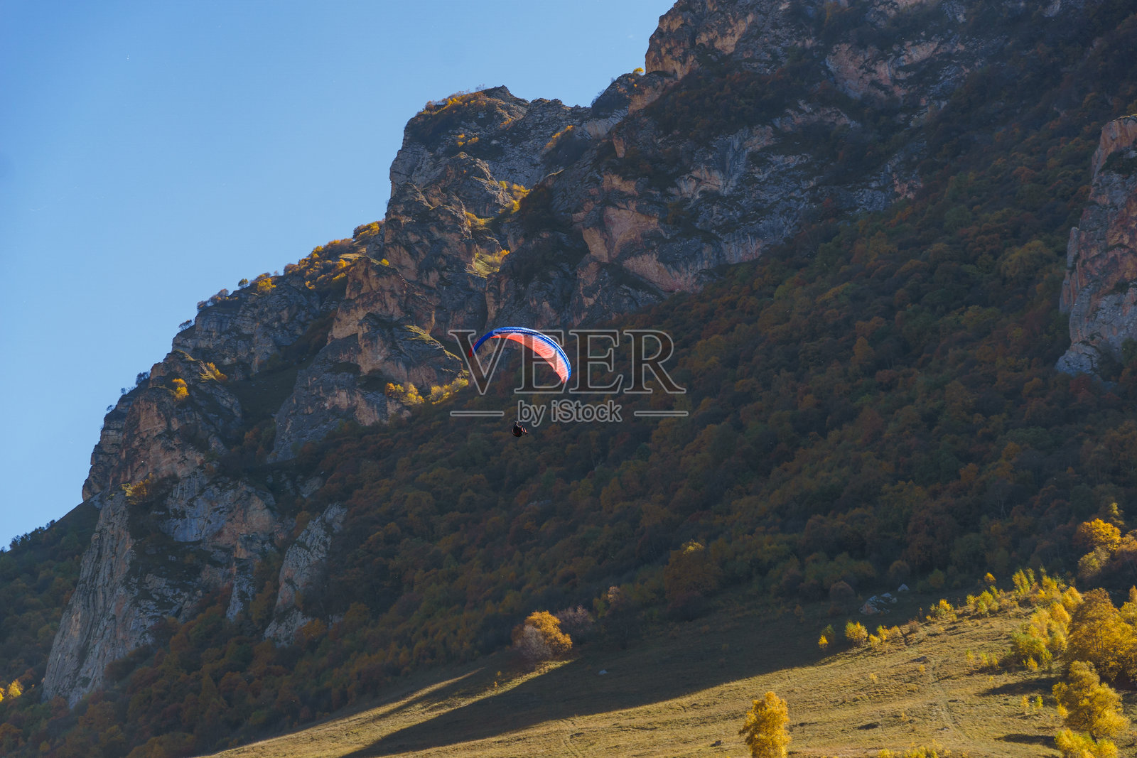 滑翔伞在郁郁葱葱的秋季森林上空宁静地漂浮,四周环绕着崎岖的悬崖和绚丽的秋叶。飞切根滑翔伞场,埃尔-秋布照片摄影图片