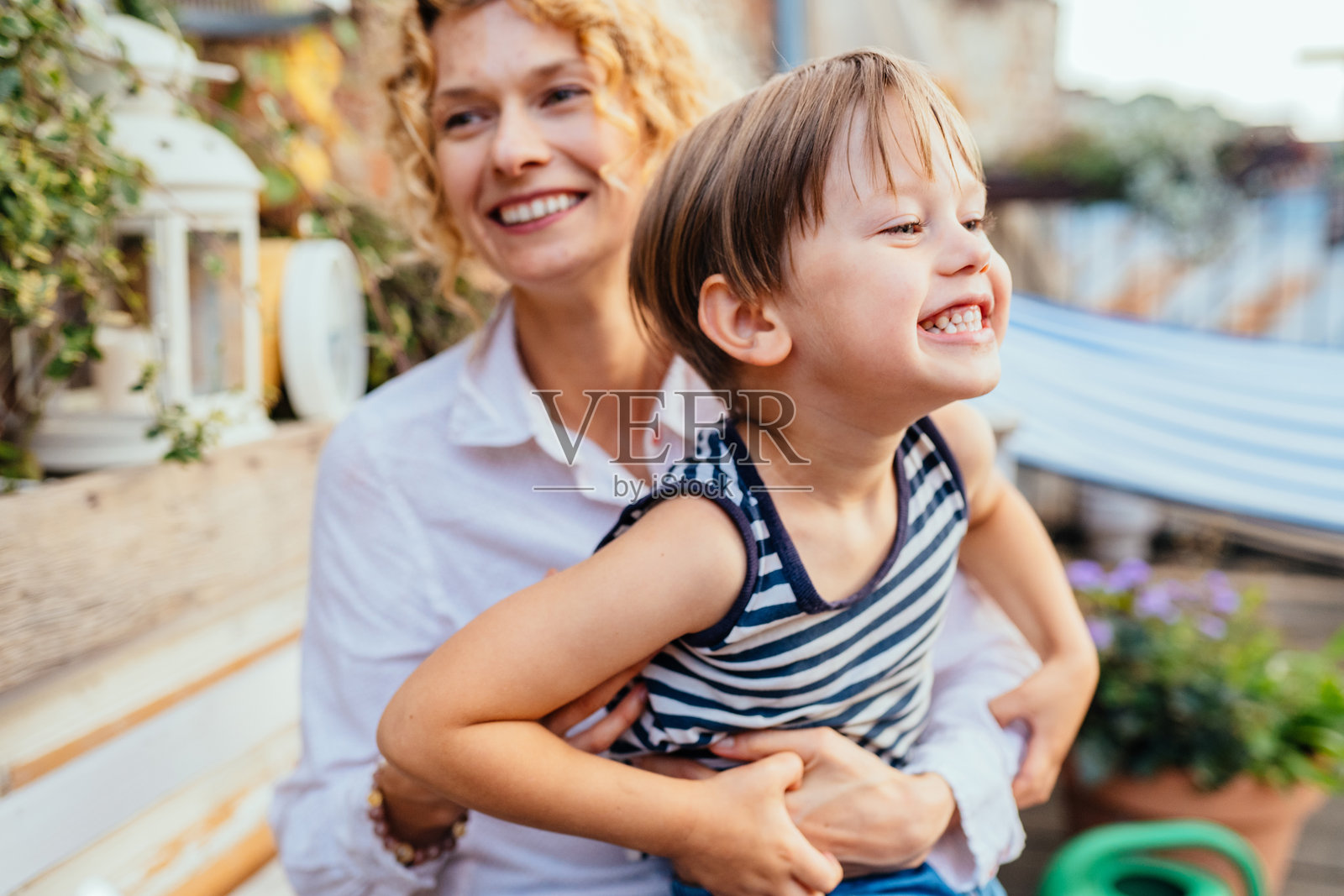 美丽的家庭肖像,快乐的欧洲母亲和儿子在夏季露台上微笑、享受和玩耍。漂亮的金发卷发女性抱着她的儿子。照片摄影图片