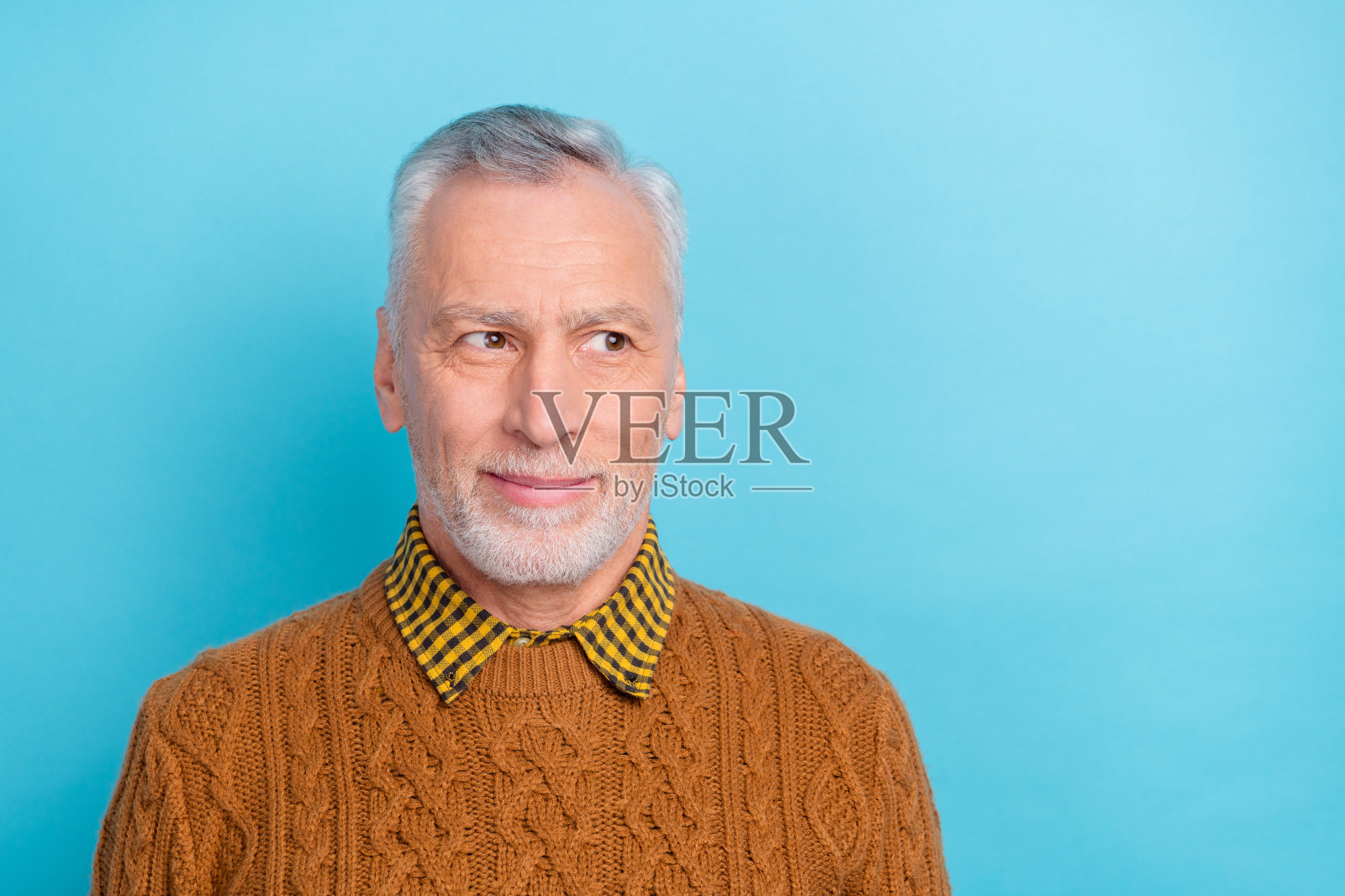 可爱的沉思老人穿着棕色毛衣,凝视空旷的空间,背景为蓝色。照片摄影图片