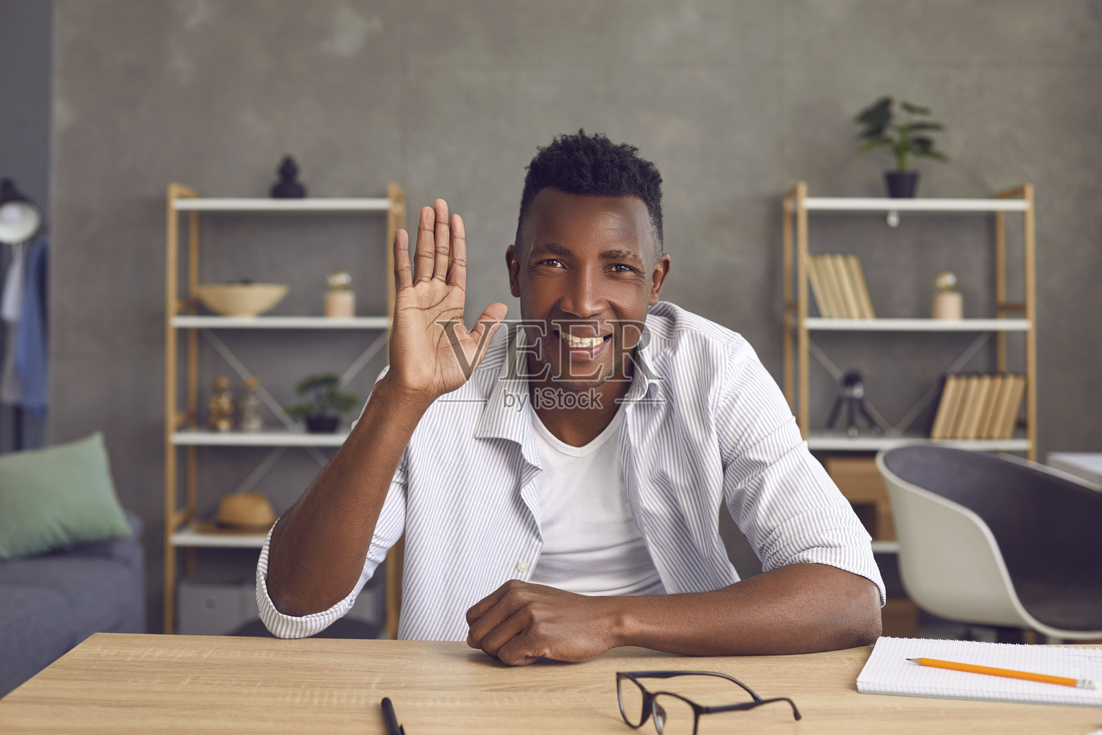 快乐的黑人学生坐在家里的书桌前,微笑着向镜头挥手。照片摄影图片