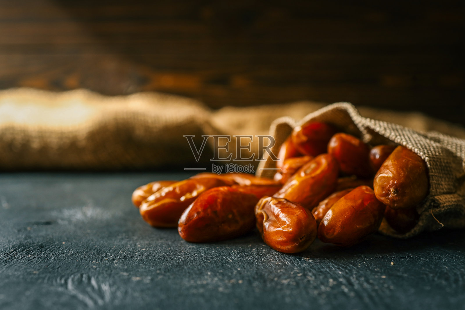 干枣从麻布袋中倾泻而出,洒落在深色表面上。这些天然的甜果富含纤维和营养,常用于健康饮食和中东美食中。照片摄影图片