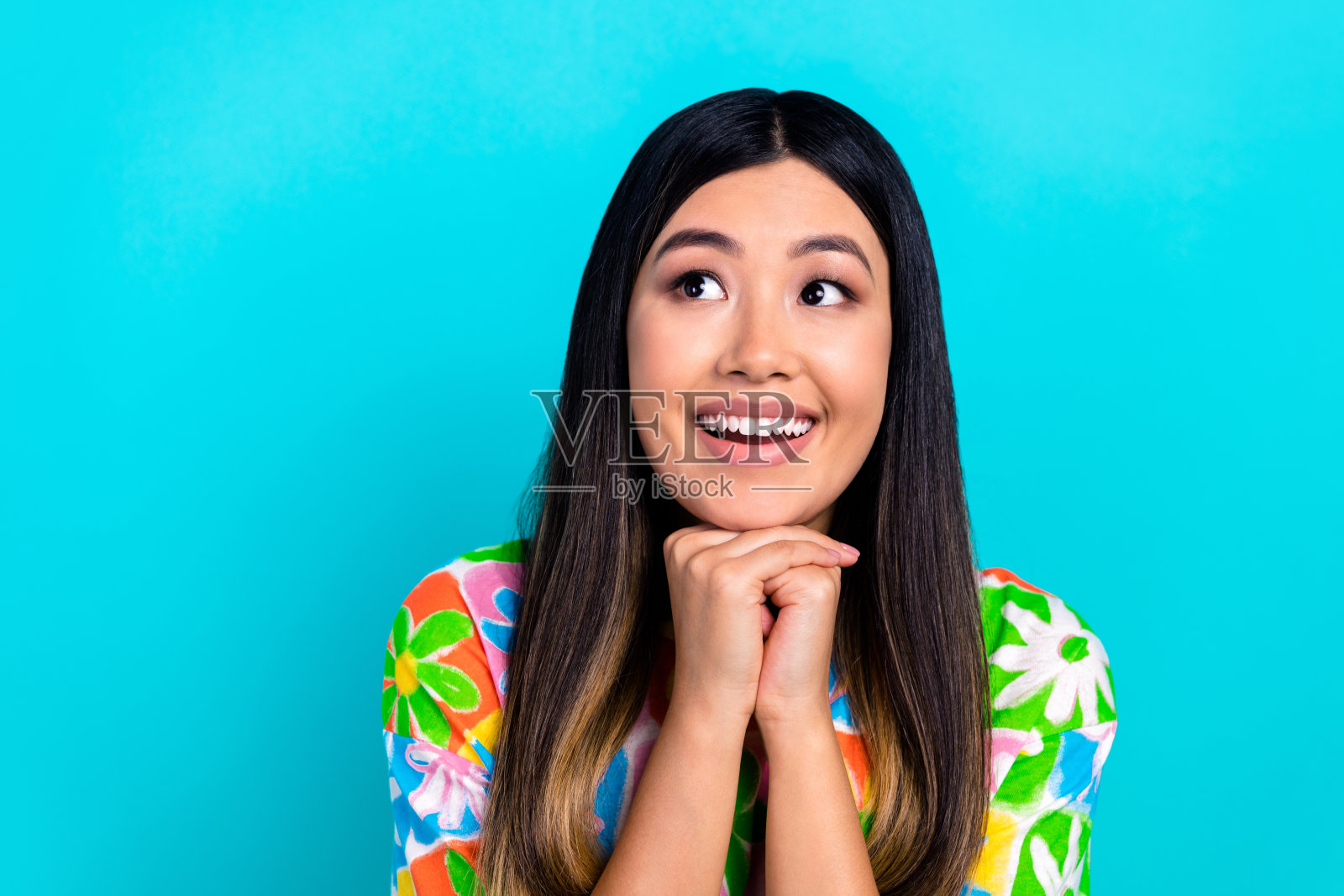 穿着花卉印花T恤的积极梦幻女性,双臂托着下巴,凝视空旷的空间,背景为蓝色。照片摄影图片