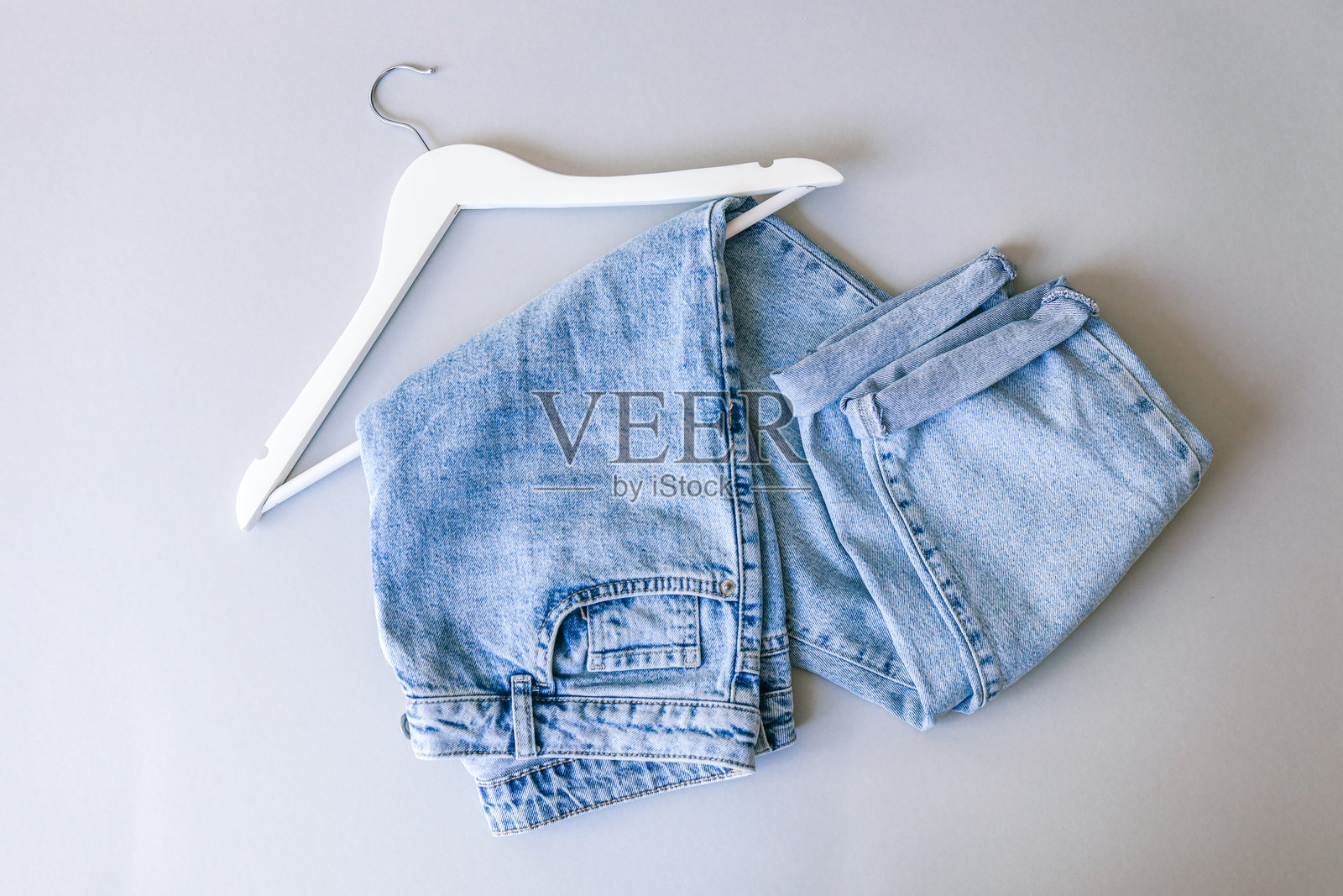 折叠的浅蓝色牛仔裤挂在白色衣架上,背景为简约的灰色。照片摄影图片