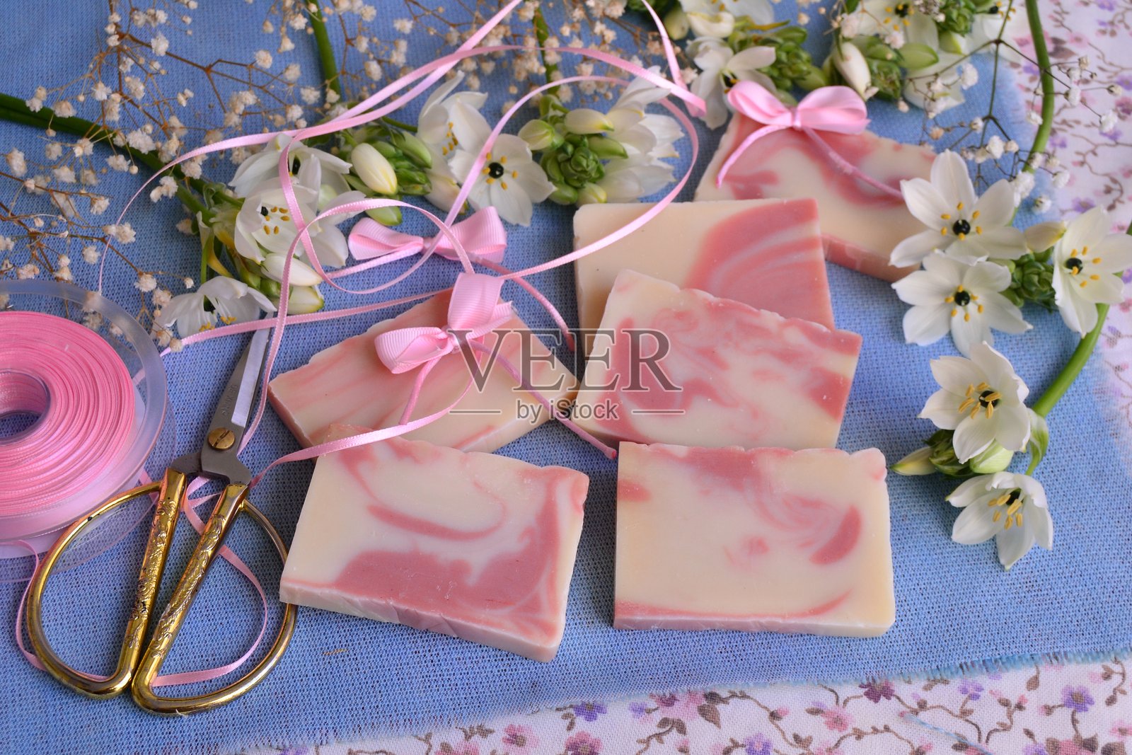 婚礼伴手礼:粉色丝带蝴蝶结的肥皂制作,背景为蓝色麻布和白色花朵,适合派对嘉宾的礼物照片摄影图片