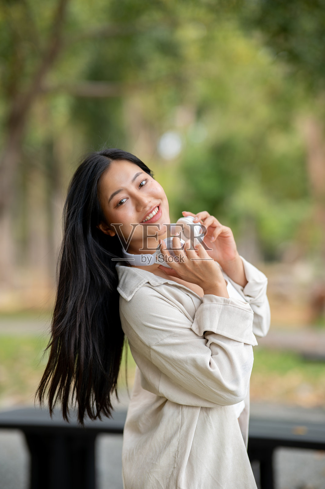 一位微笑的亚洲女性在公园里手持耳机,凝视着镜头。照片摄影图片