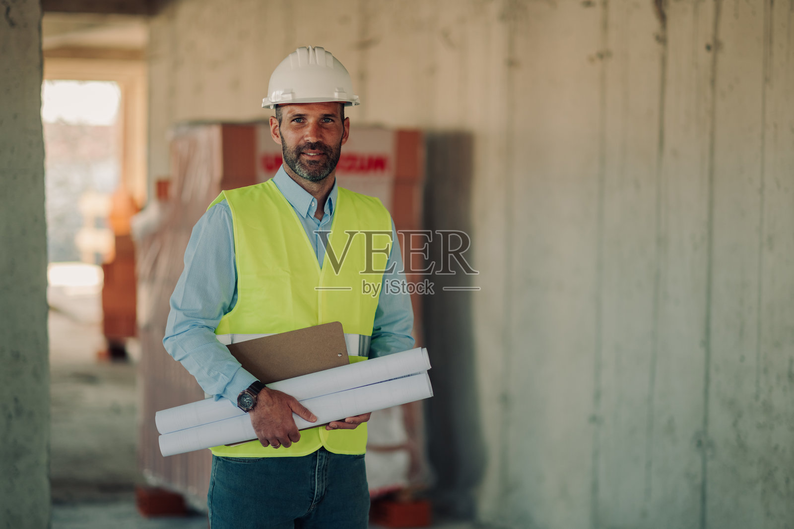 微笑的工程师在建筑工地上手持蓝图和夹板照片摄影图片