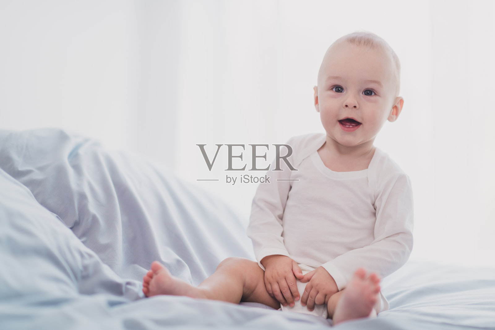 可爱的小宝宝穿着白衬衫,坐在柔软舒适的床上,微笑着,室内家居环境。照片摄影图片