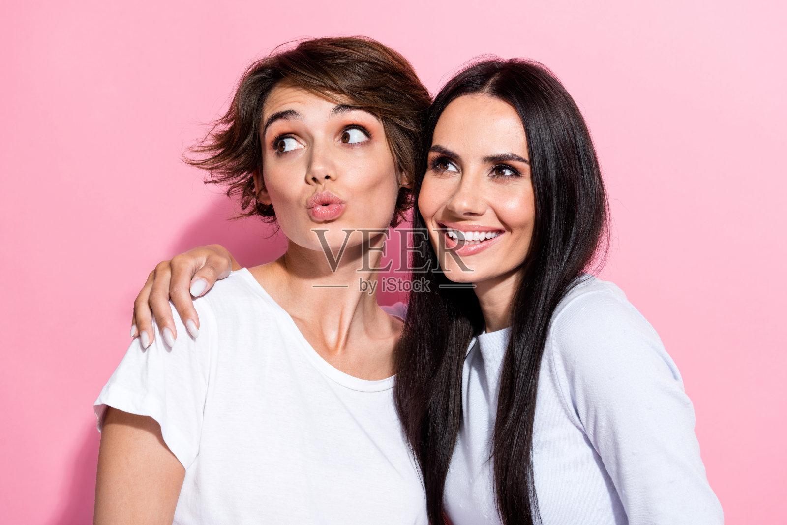 穿着白色时尚服装的可爱女孩们微笑着,嘟嘴凝视空旷的空间,背景为粉色,特别优惠。照片摄影图片