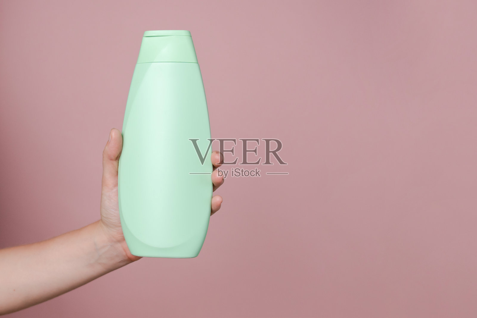 优雅的手握着轻便的洗发水瓶,背景为纯粉色。适用于化妆品产品的包装,您的品牌,水疗,美容。留有文字空间。照片摄影图片