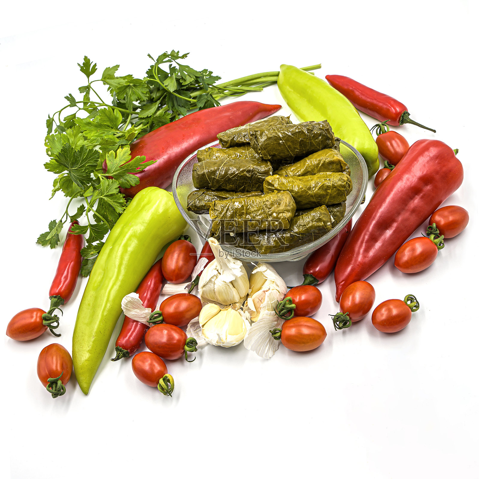 新鲜蔬菜的葡萄叶卷。色彩丰富、美味可口的组合,背景为白色,葡萄叶卷盛放在玻璃碗中,周围环绕着新鲜蔬菜和调料。照片摄影图片