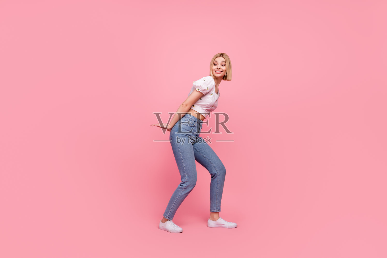 全身照,兴奋搞笑、强大勤奋的女士手持巨大无敌物体,凝视空旷的空间,背景为粉色。照片摄影图片