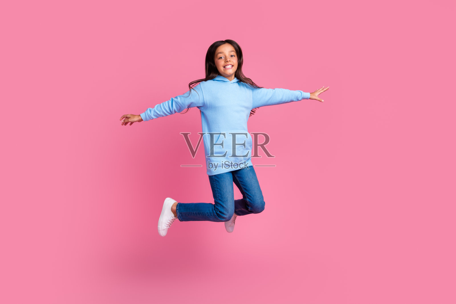 充满活力的年轻女孩穿着休闲服装,在鲜艳的粉色背景下欢快地跳跃,展现出魅力和快乐。照片摄影图片