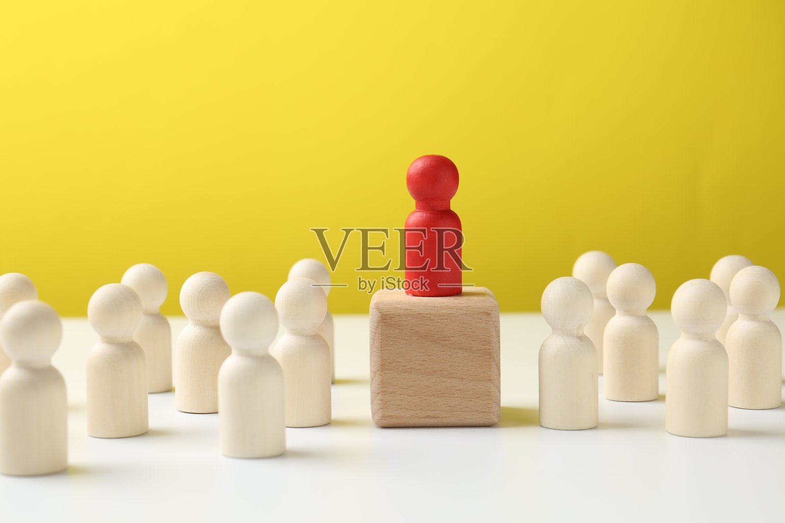 人形围绕着木块,顶部有一个红色人形,背景为黄色。这是一个竞争的概念。照片摄影图片