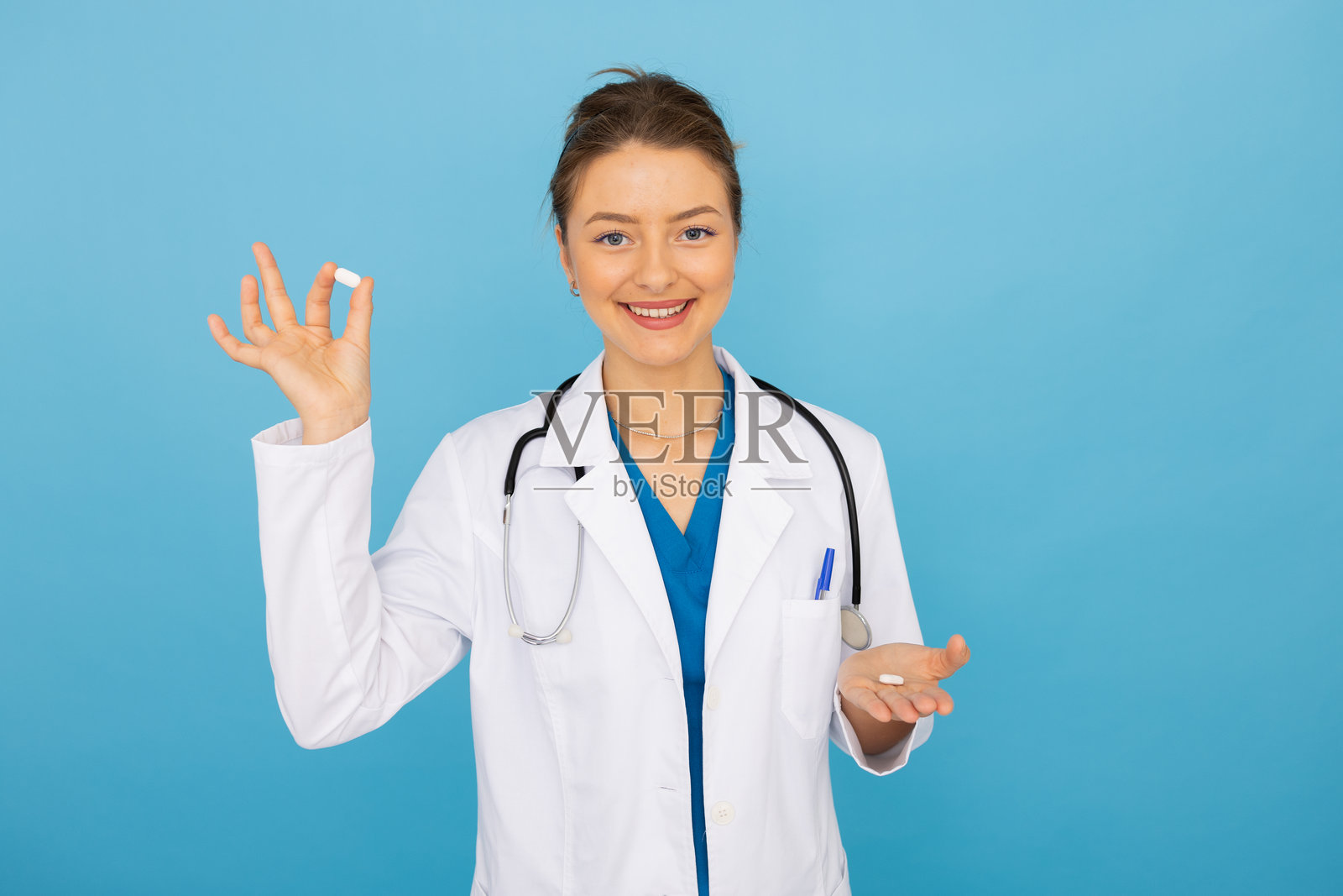女医生在蓝色背景下微笑并展示一颗药丸照片摄影图片