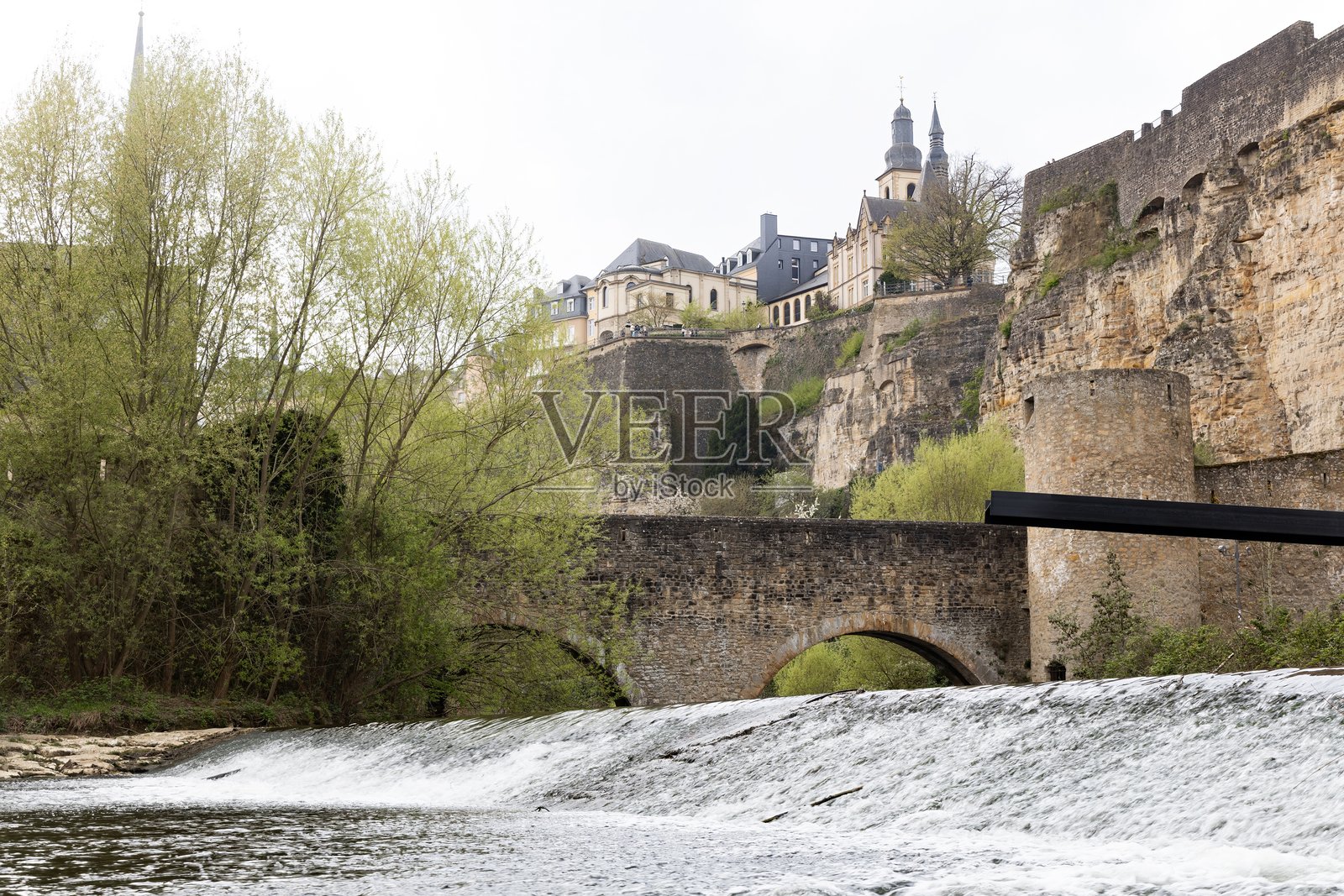 卢森堡市的景观,云彩、教堂尖塔、拱形桥和河边步道。照片摄影图片