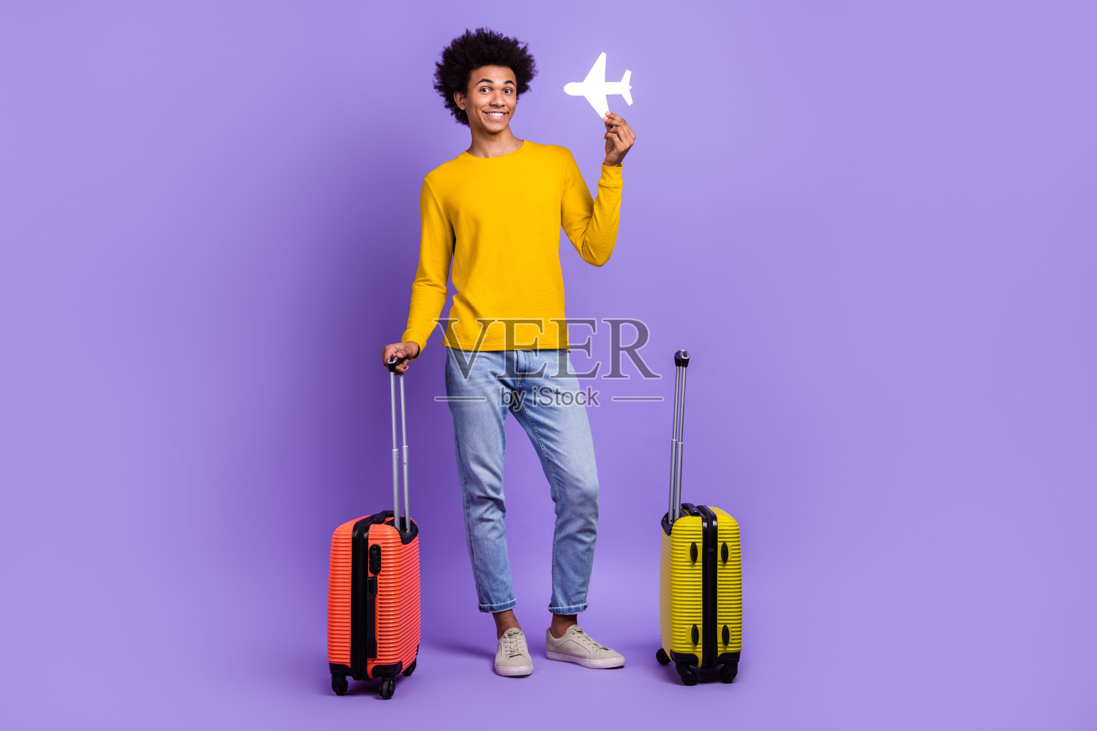 全身肖像,愉快积极的人手持小纸飞机和行李箱,背景为紫色。照片摄影图片