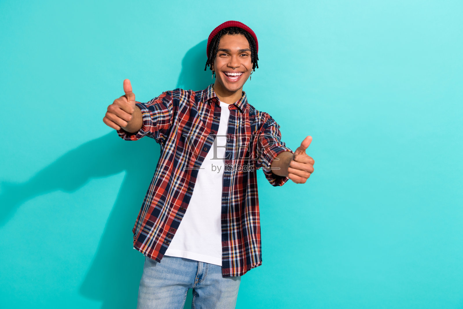 帅气年轻男子的照片肖像,双手竖起大拇指,穿着时尚的格子服装,背景为青色。照片摄影图片