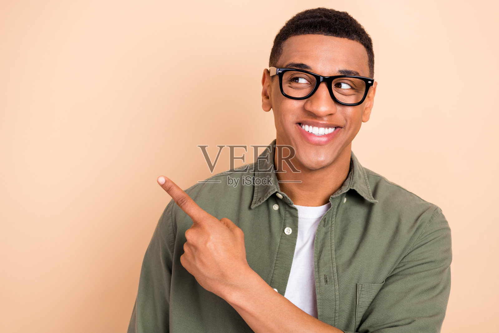 年轻人面带灿烂微笑,手指指向空白处,背景为米色。照片摄影图片