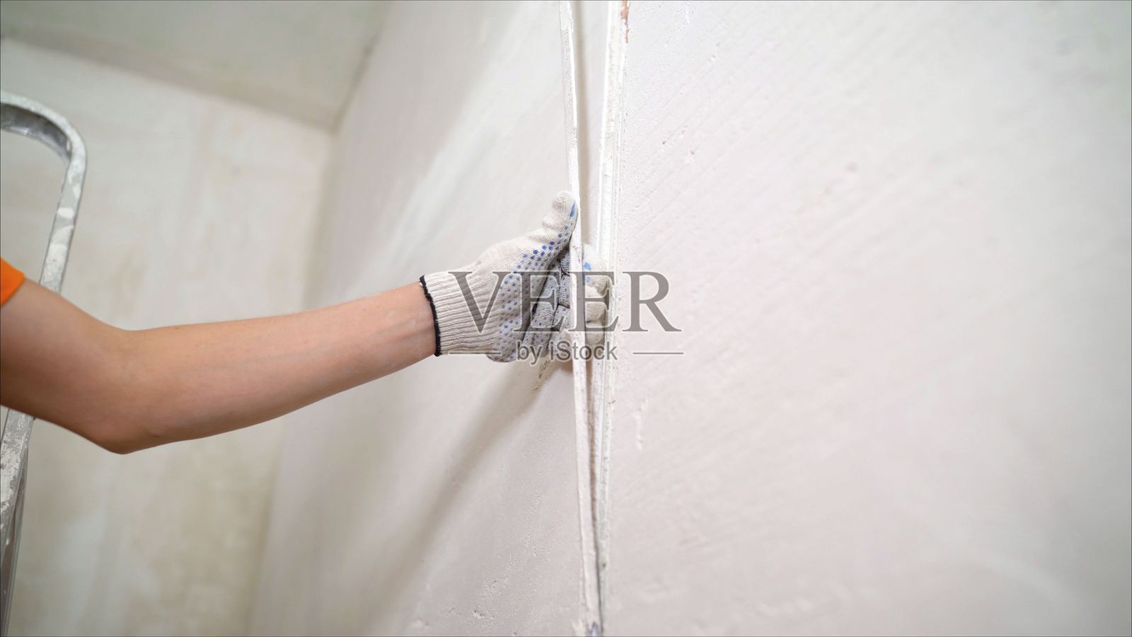 建筑工人正在对墙壁进行抹灰的特写镜头。墙内有金属标尺。一名工人在涂抹完抹灰后,从墙壁中拔出金属导轨。拆除装饰条。照片摄影图片