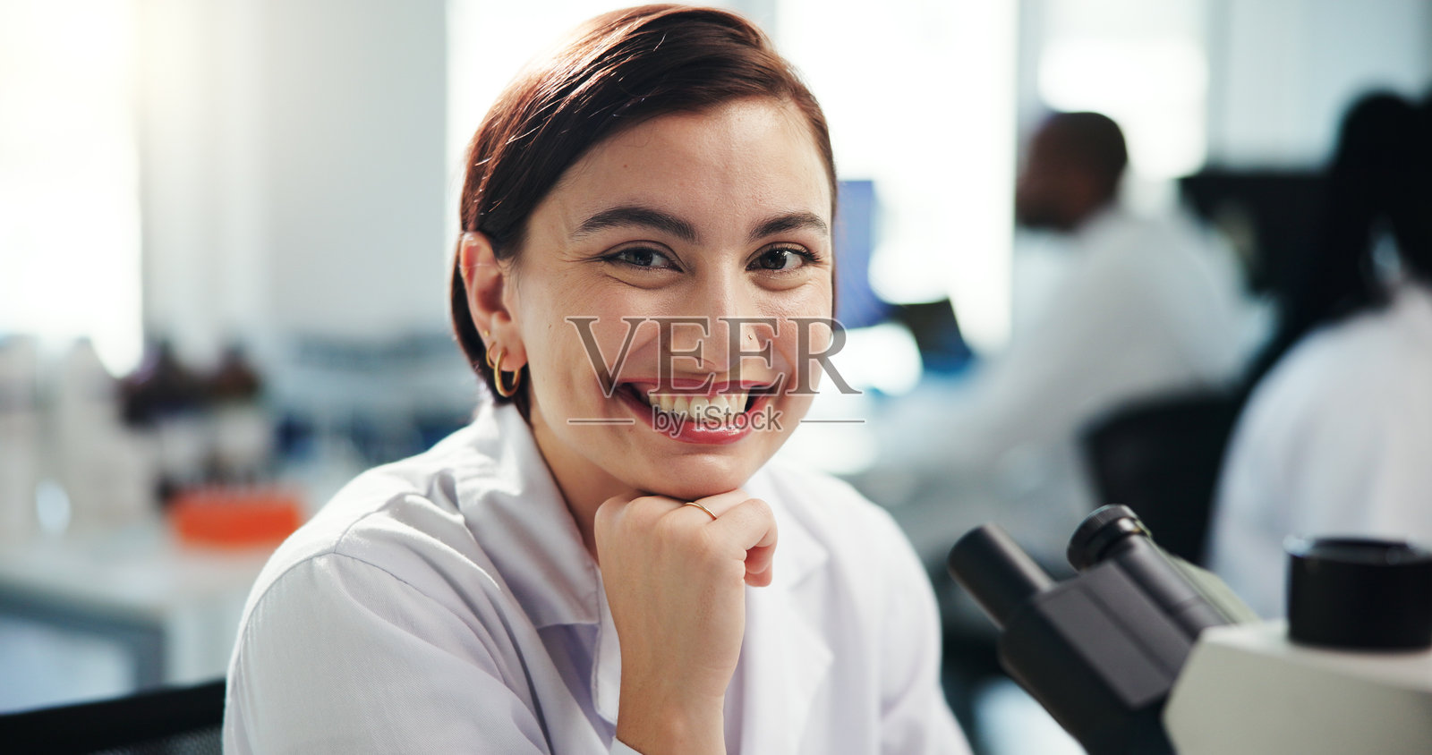 实验室中微笑的女性科学家与显微镜进行医学研究,实验和关于我们的介绍。她自信地从事生物技术,研究病毒和样本测试以开发疫苗。照片摄影图片
