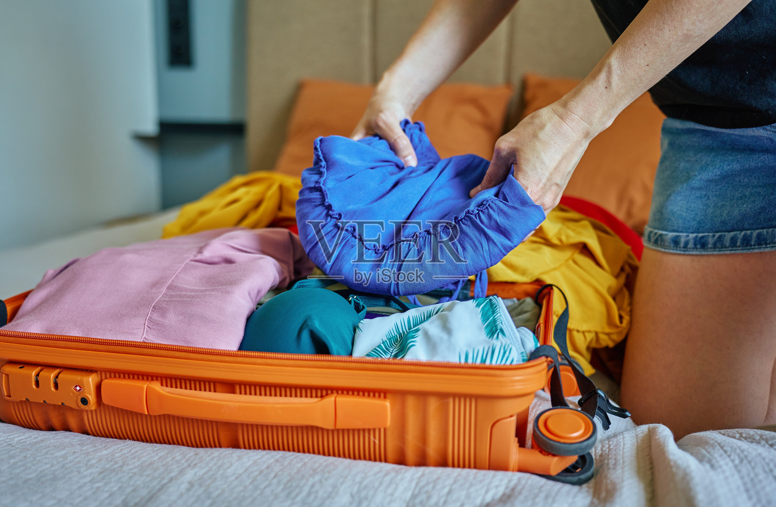 女人正在把五颜六色的衣服装进橙色行李箱,为度假做准备照片摄影图片