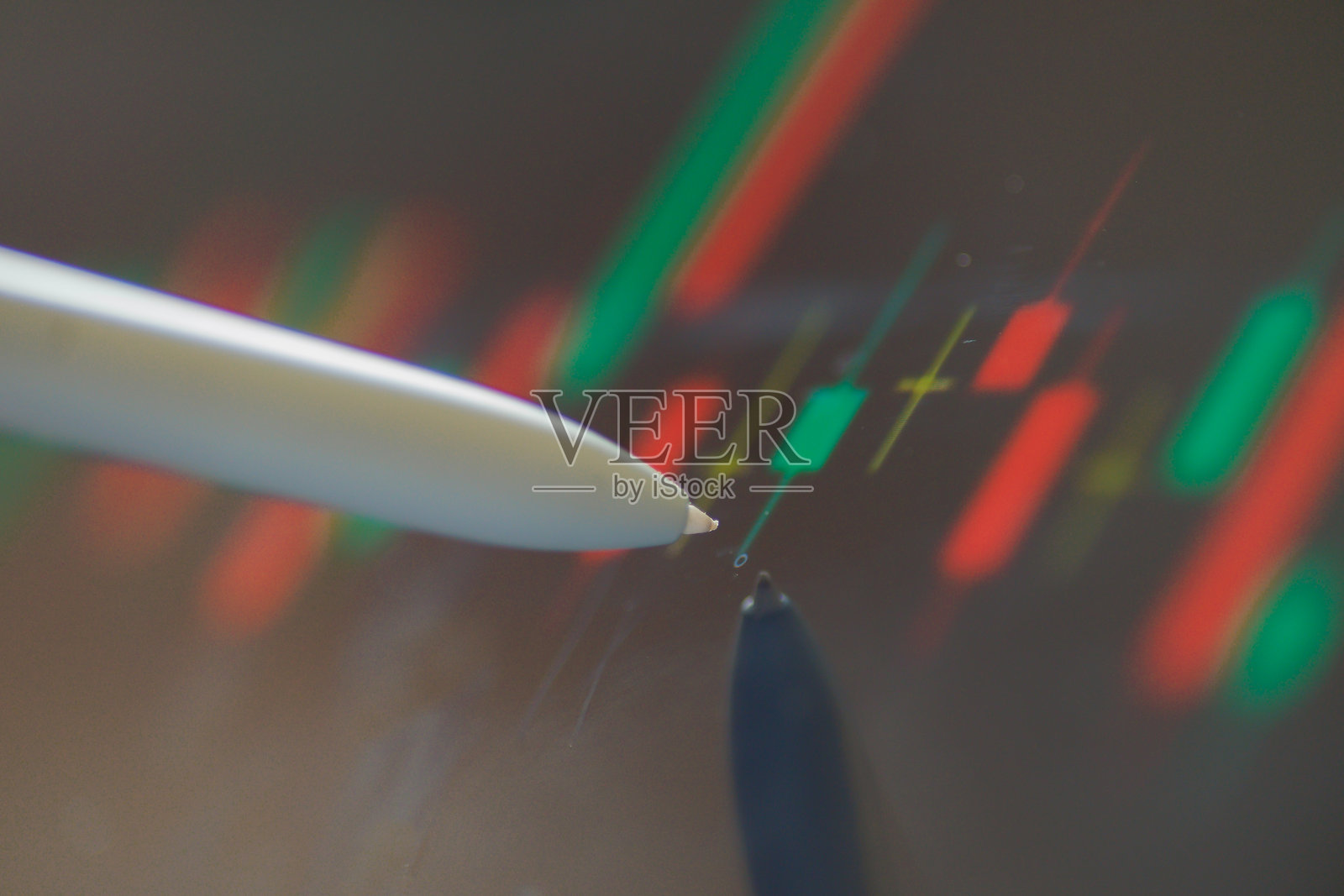 一支笔尖指向显示绿色和红色股市图表波动的屏幕照片摄影图片