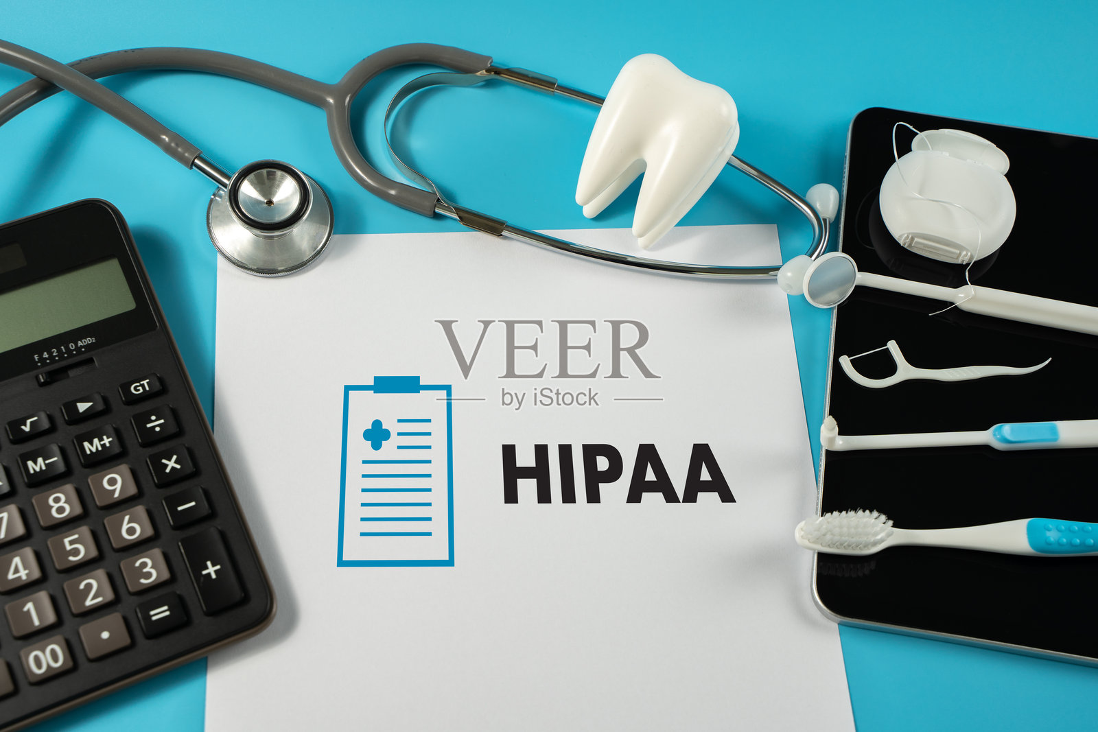 一台带有“HIPAA”的笔记本电脑,周围有牙科工具、听诊器、计算器和HIPAA文件,蓝色背景,突出强调。照片摄影图片