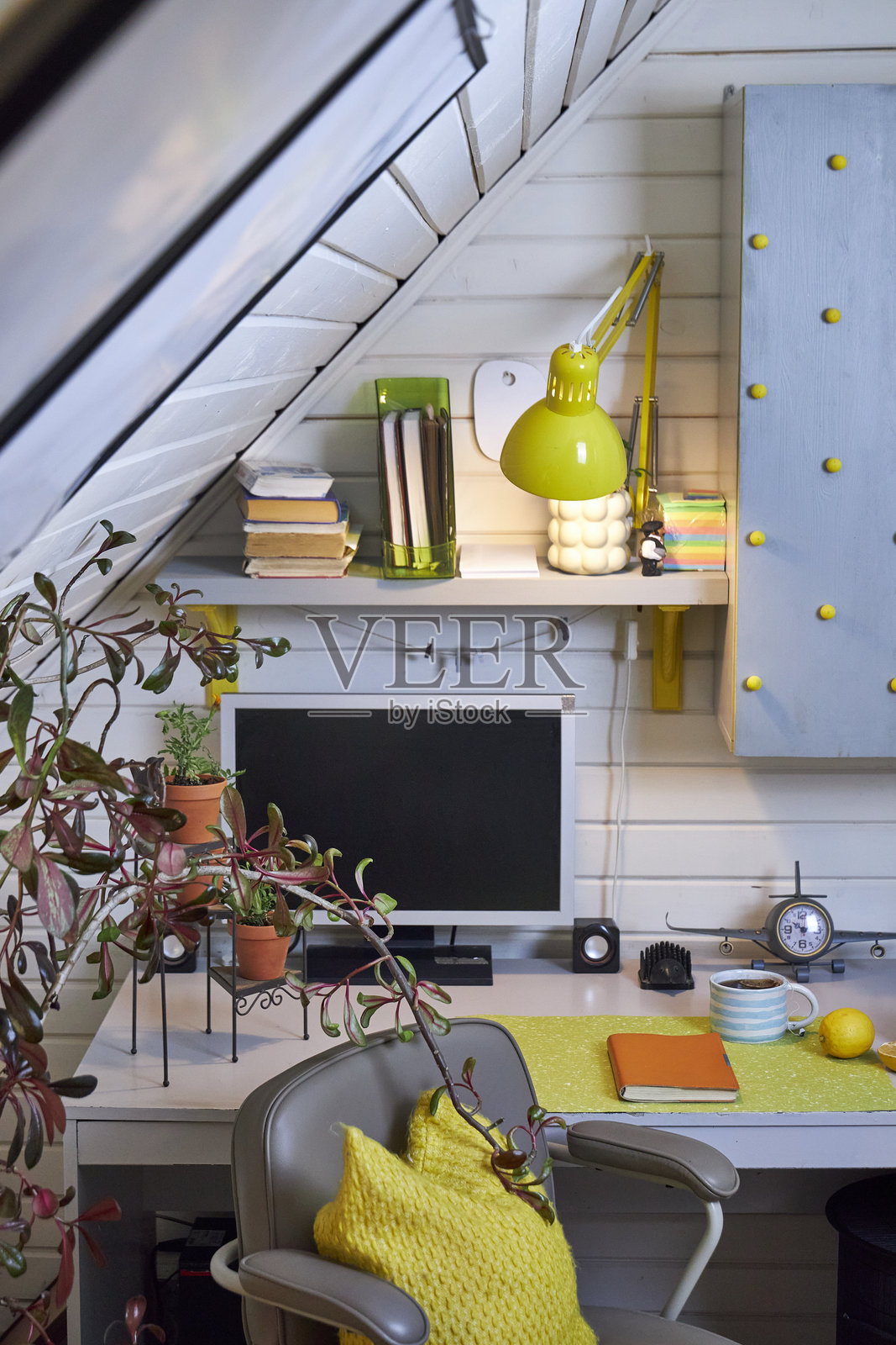 一个阁楼房间的工作空间,配有灰色旋转椅和一张带电脑的桌子,装饰以灰色调和黄色点缀。照片摄影图片