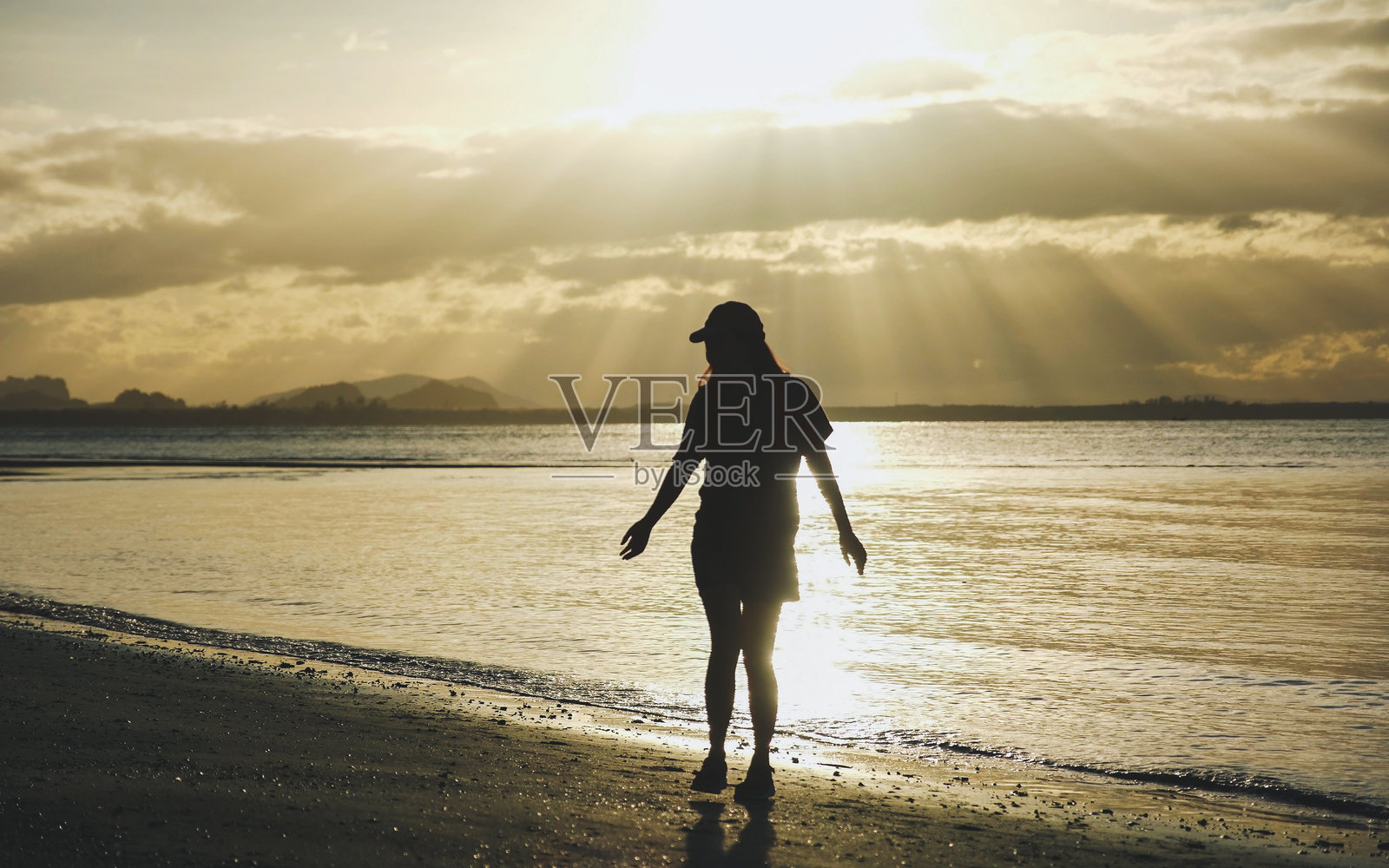 早晨在海滩上站着的戴帽子女性的剪影照片摄影图片