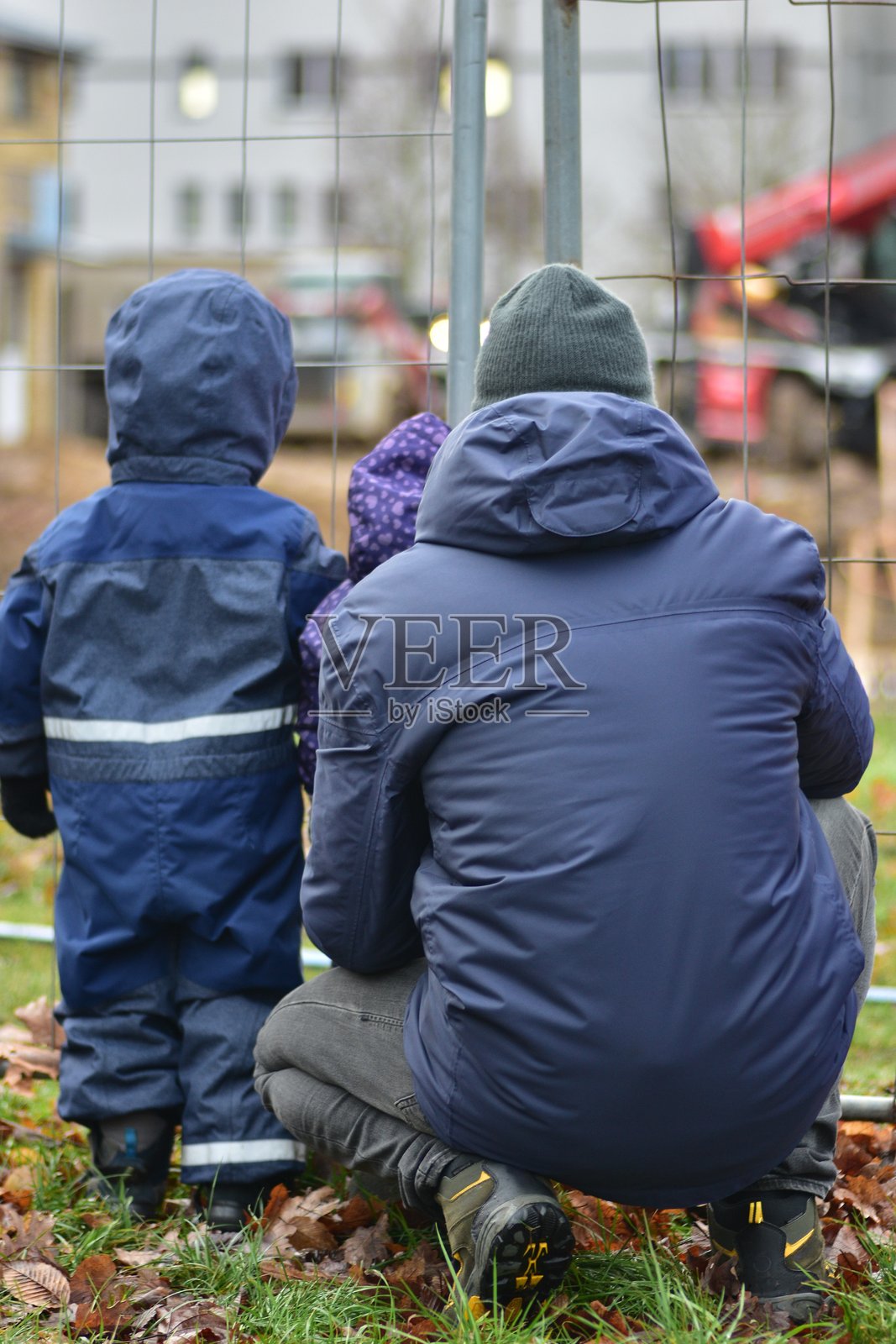 小男孩、小女孩和他们的爸爸透过围栏看向施工现场。好奇的孩子们和爸爸在观察施工过程。照片摄影图片