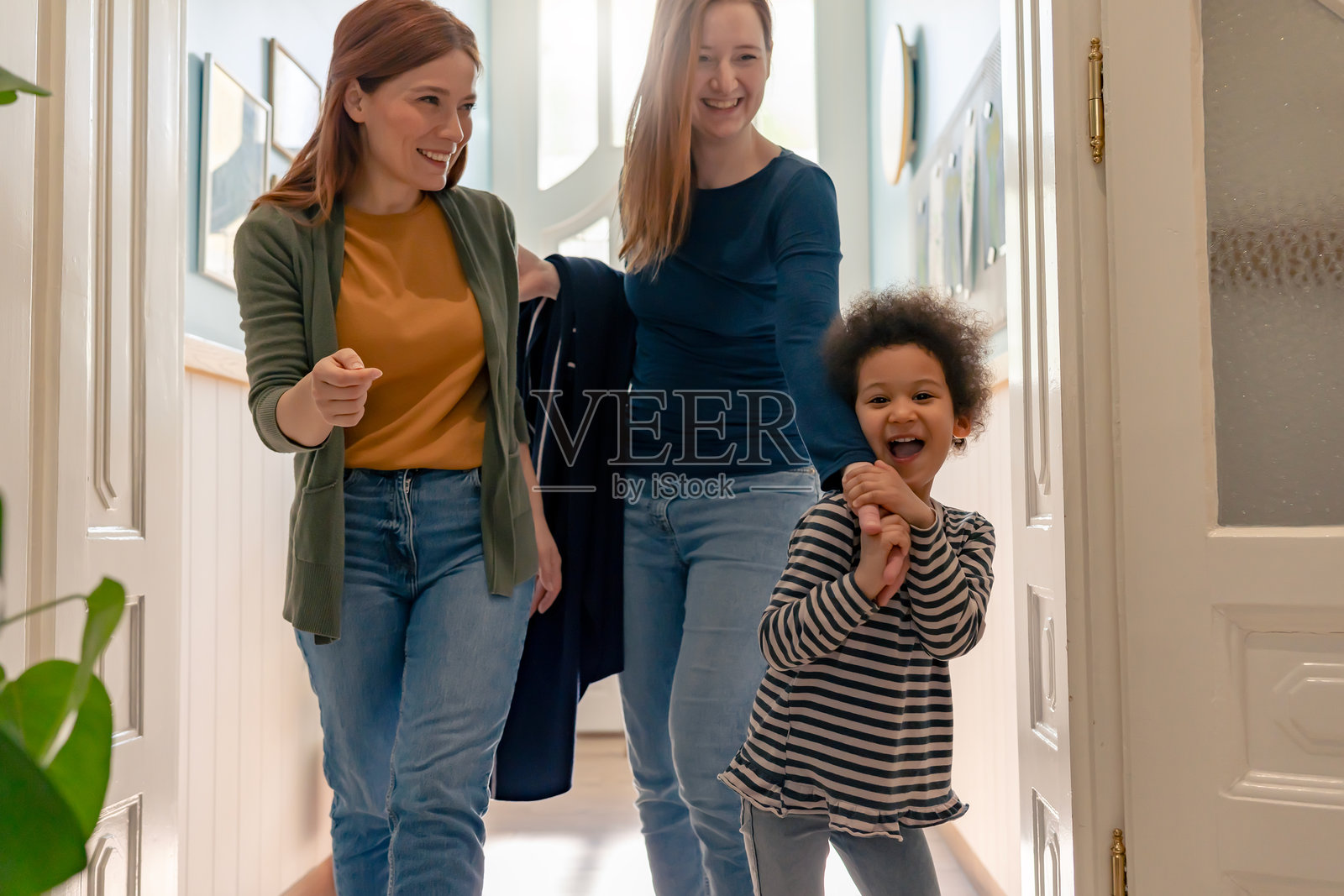 快乐的学龄前儿童与母亲和老师一起走在走廊上,分享着温暖、友好和多元化的早期教育环境中的快乐时光。照片摄影图片