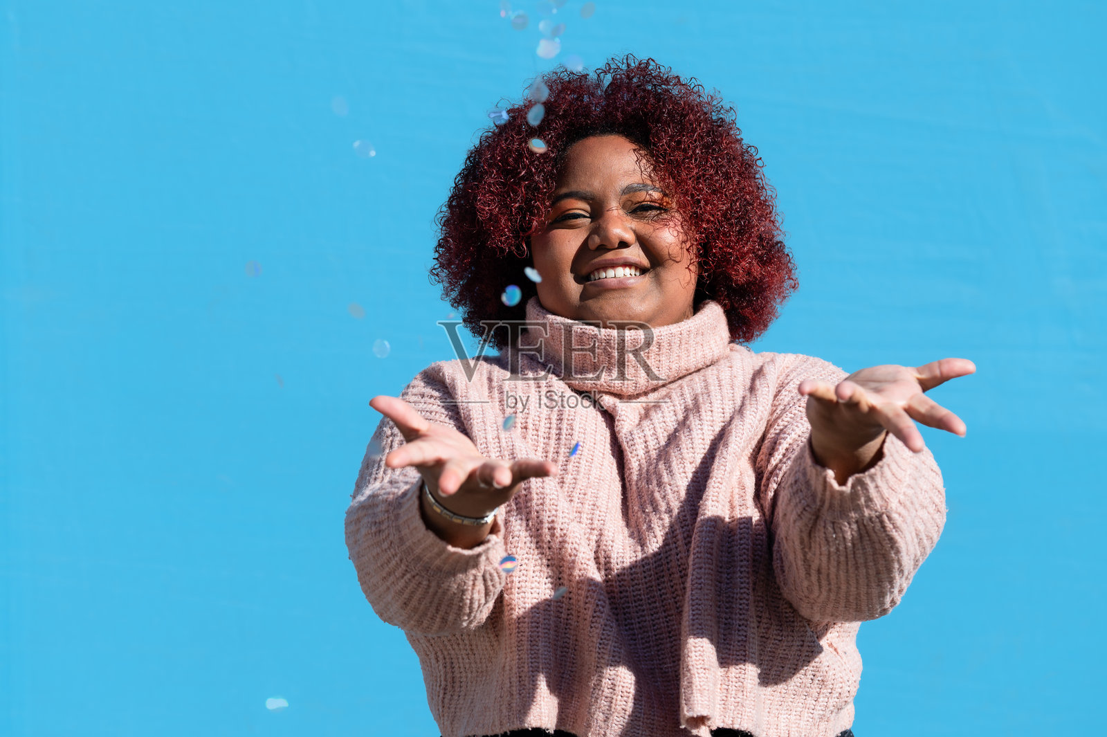 年轻女性在蓝色背景下享受飘落的五彩纸屑乐趣照片摄影图片