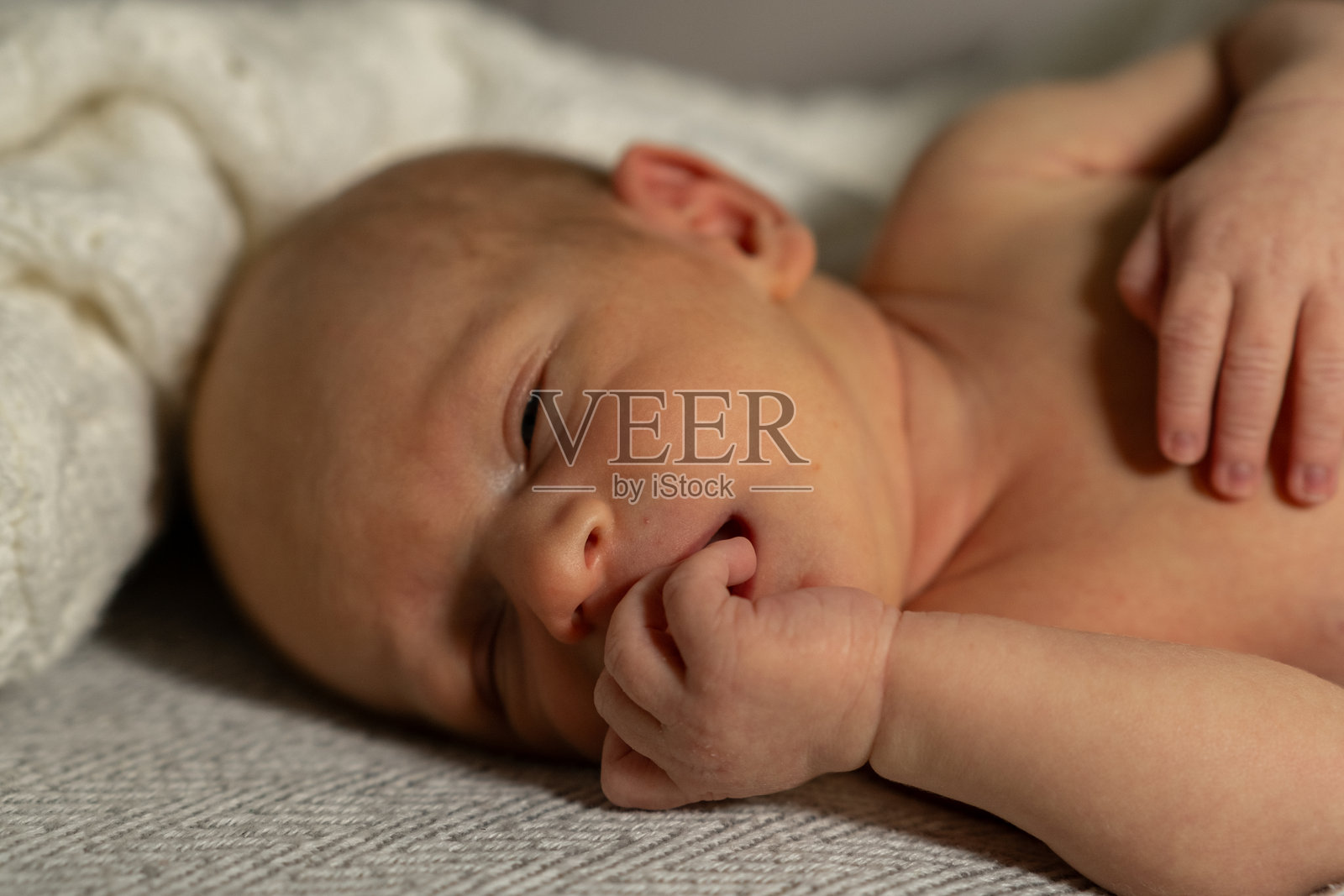 婴儿躺在柔软的毯子上,安静地做着梦,手指放在嘴里,温暖的室内环境中沐浴在晨光中。照片摄影图片