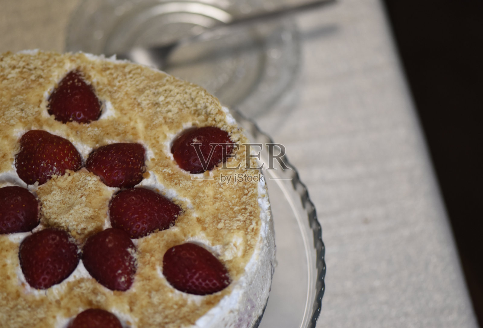 一块放有草莓的蛋糕,背景中有碟子和叉子。照片摄影图片