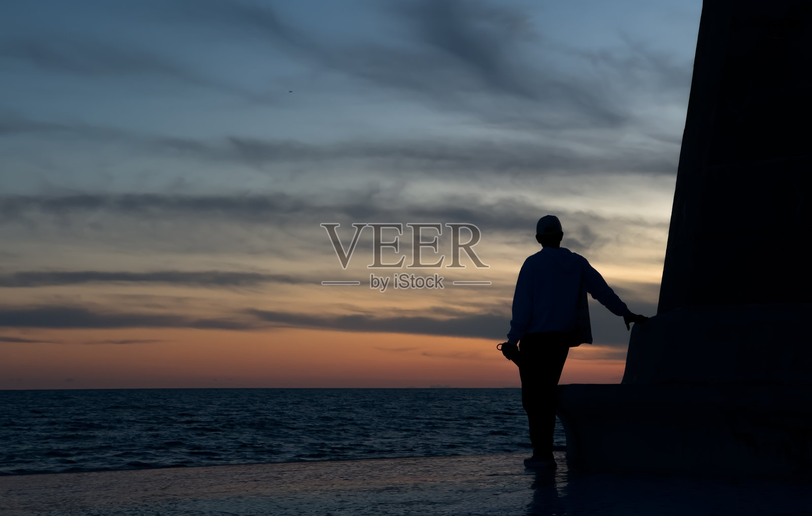 一个男人站在建筑旁边,凝视着日落的剪影照片摄影图片