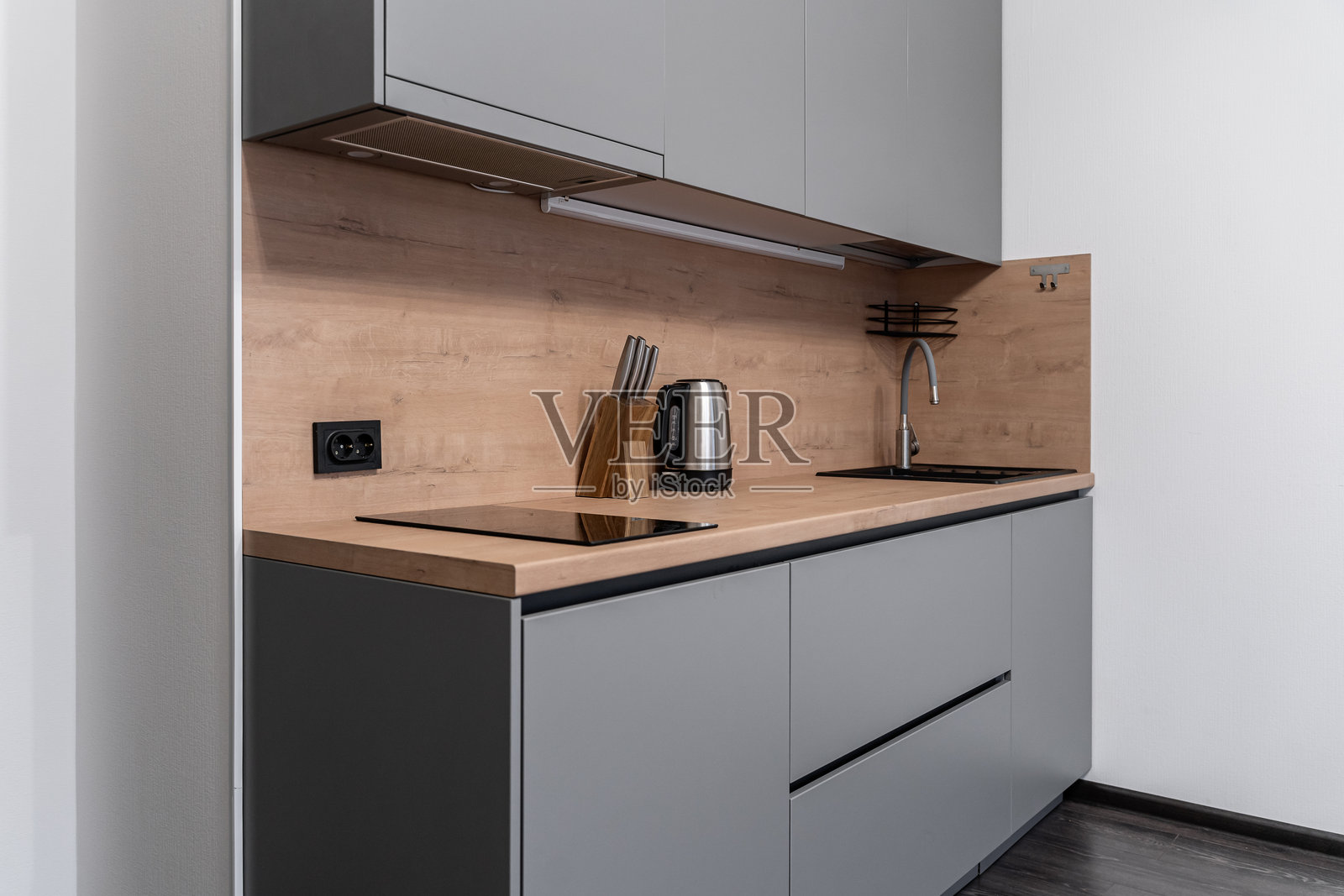 小型现代厨房位于单间公寓内。时尚的灰色嵌入式厨房配有木质台面和背板。嵌入式家具。电磁炉。不锈钢电器。厨房单元。照片摄影图片